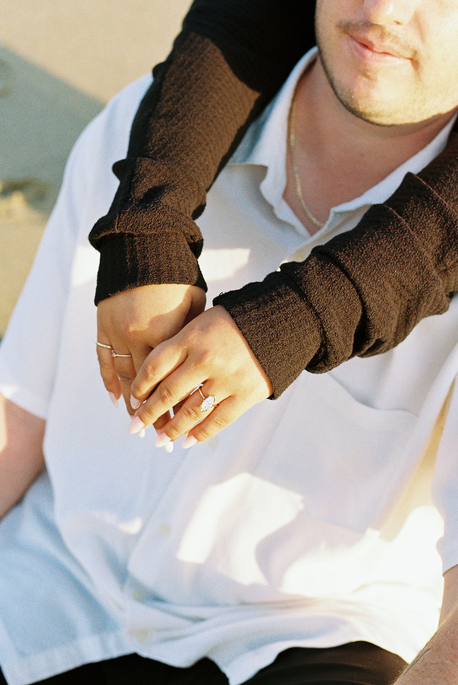 Close-up of hands clasped together wearing brown gloves and white clothing in sunlight.