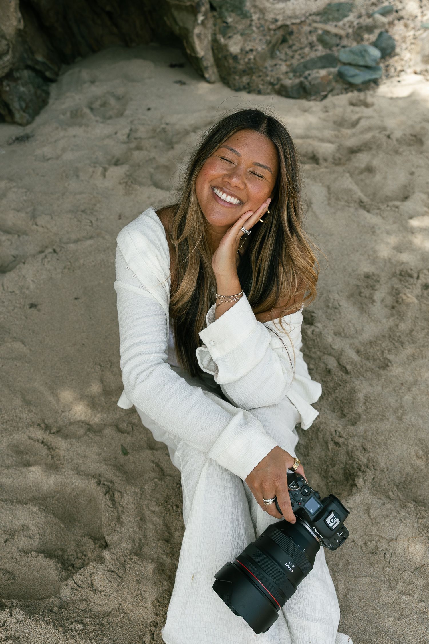 A photographer in a white outfit lies on a rocky surface while taking pictures and laughing joyfully.
