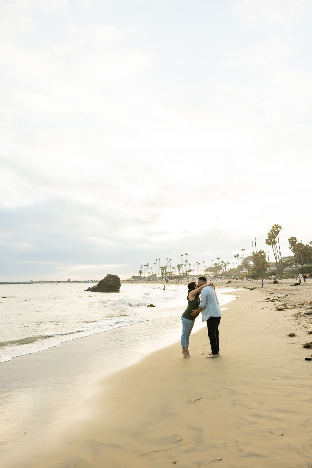 Two people walk along a serene beach at sunset with palm trees visible in the background.