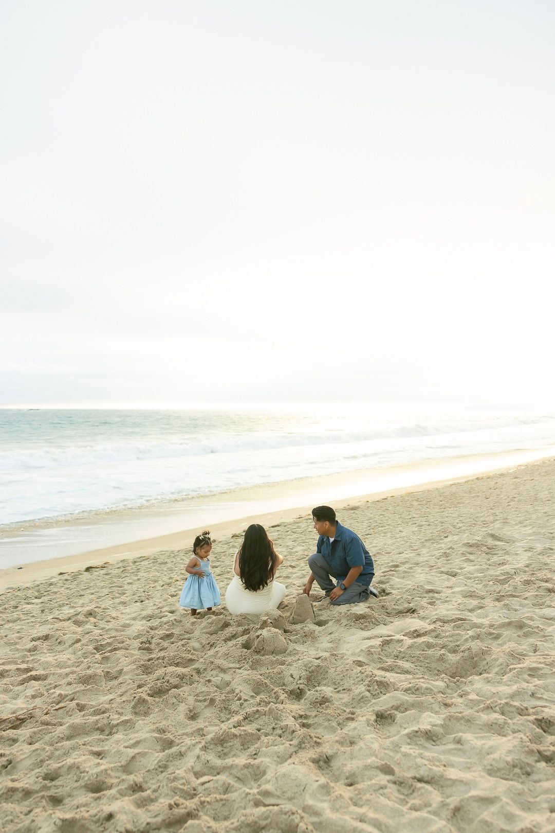 A small group plays together in the sand on a peaceful beach during sunset with ocean waves in the background.