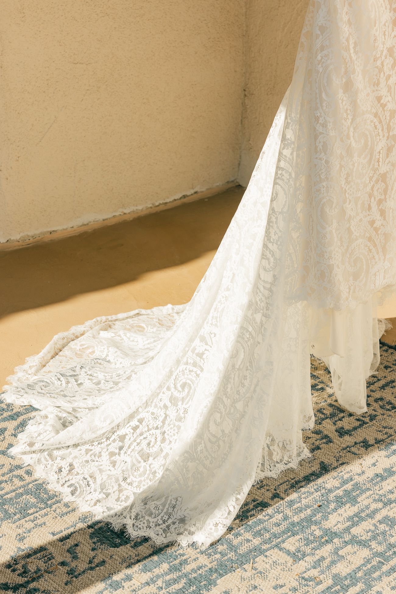 Delicate white lace wedding dress train flowing over a patterned blue carpet.