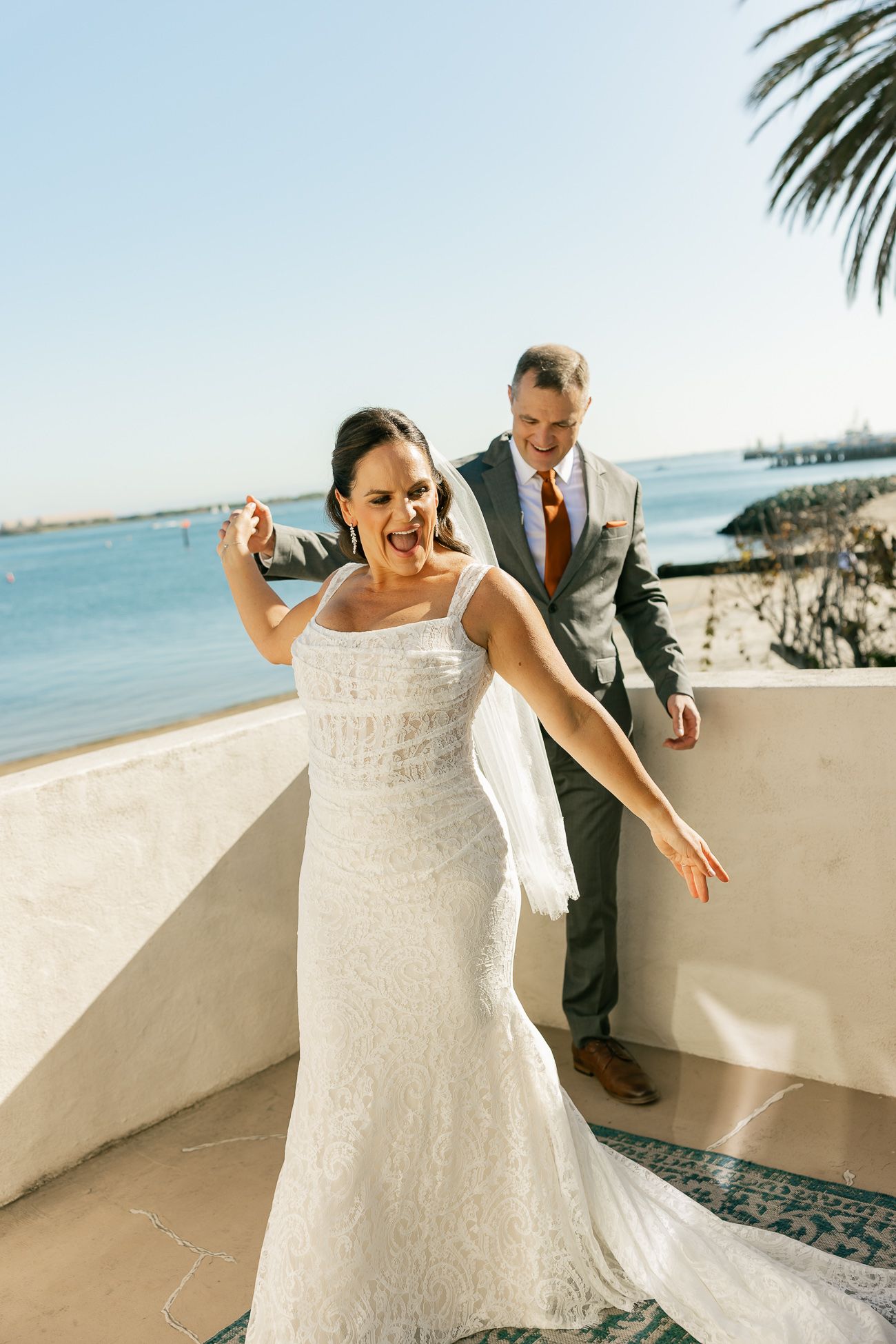 Joyful bride and groom sharing a candid moment on a sunny beachfront balcony.