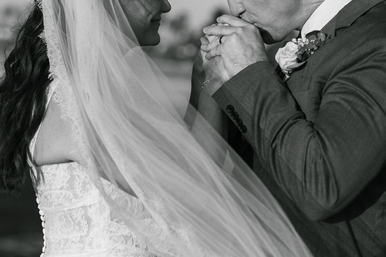 A black and white closeup of newlyweds holding hands showcasing wedding attire details.