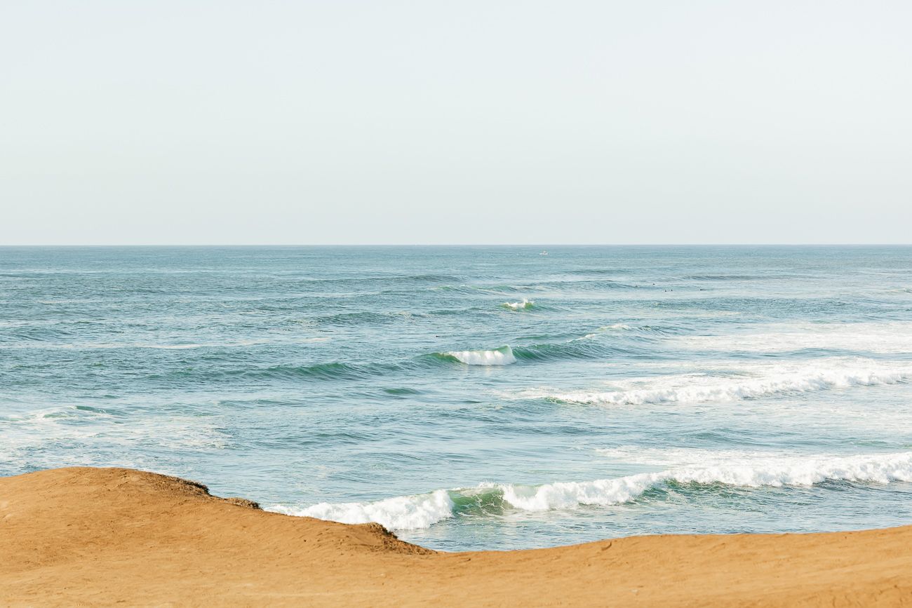 Scenic ocean view with blue waves crashing against sandy beach under bright sky.