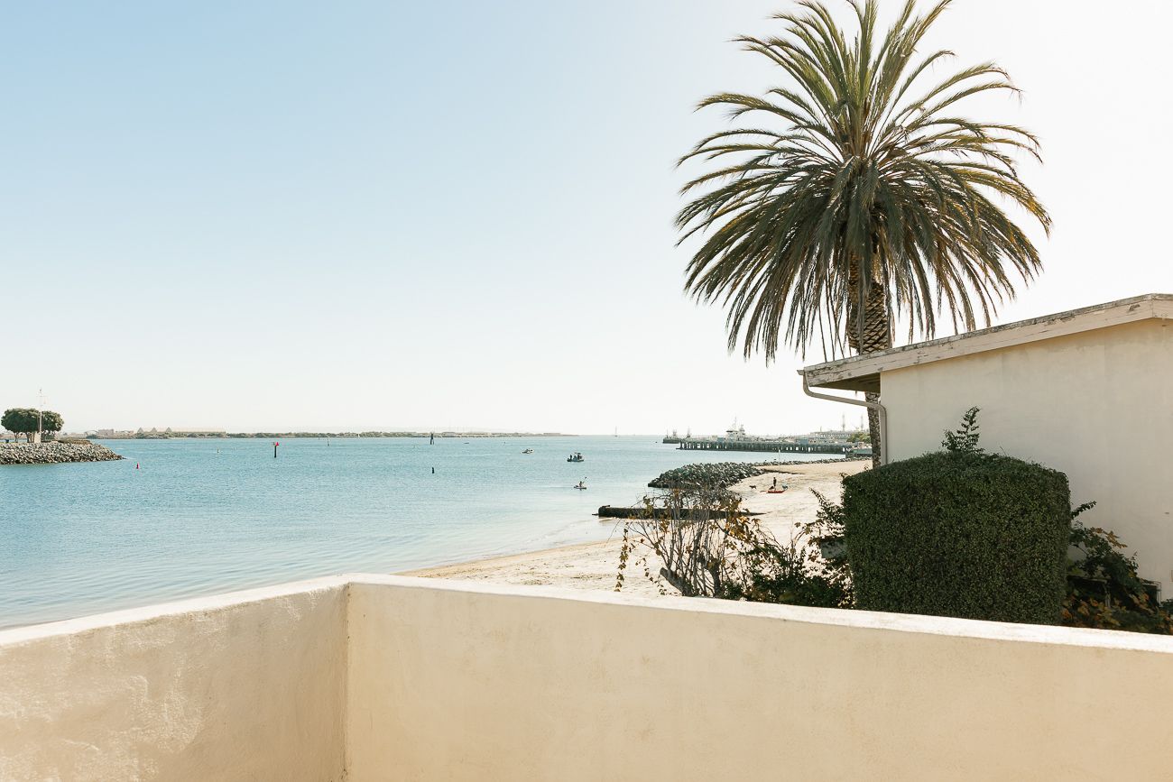 Beachfront balcony view overlooking calm blue waters with a palm tree and white building in Sainte-Marie, France.