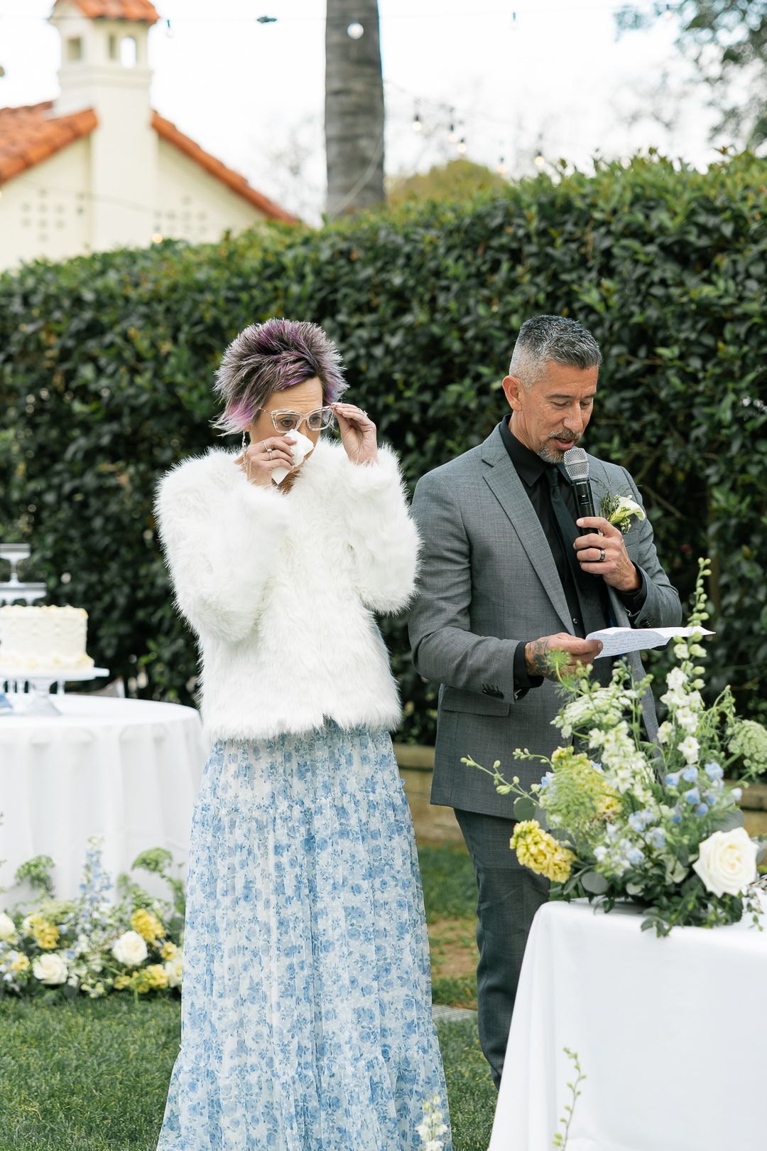 A couple shares a playful moment with cotton candy at an outdoor garden party with floral decorations.