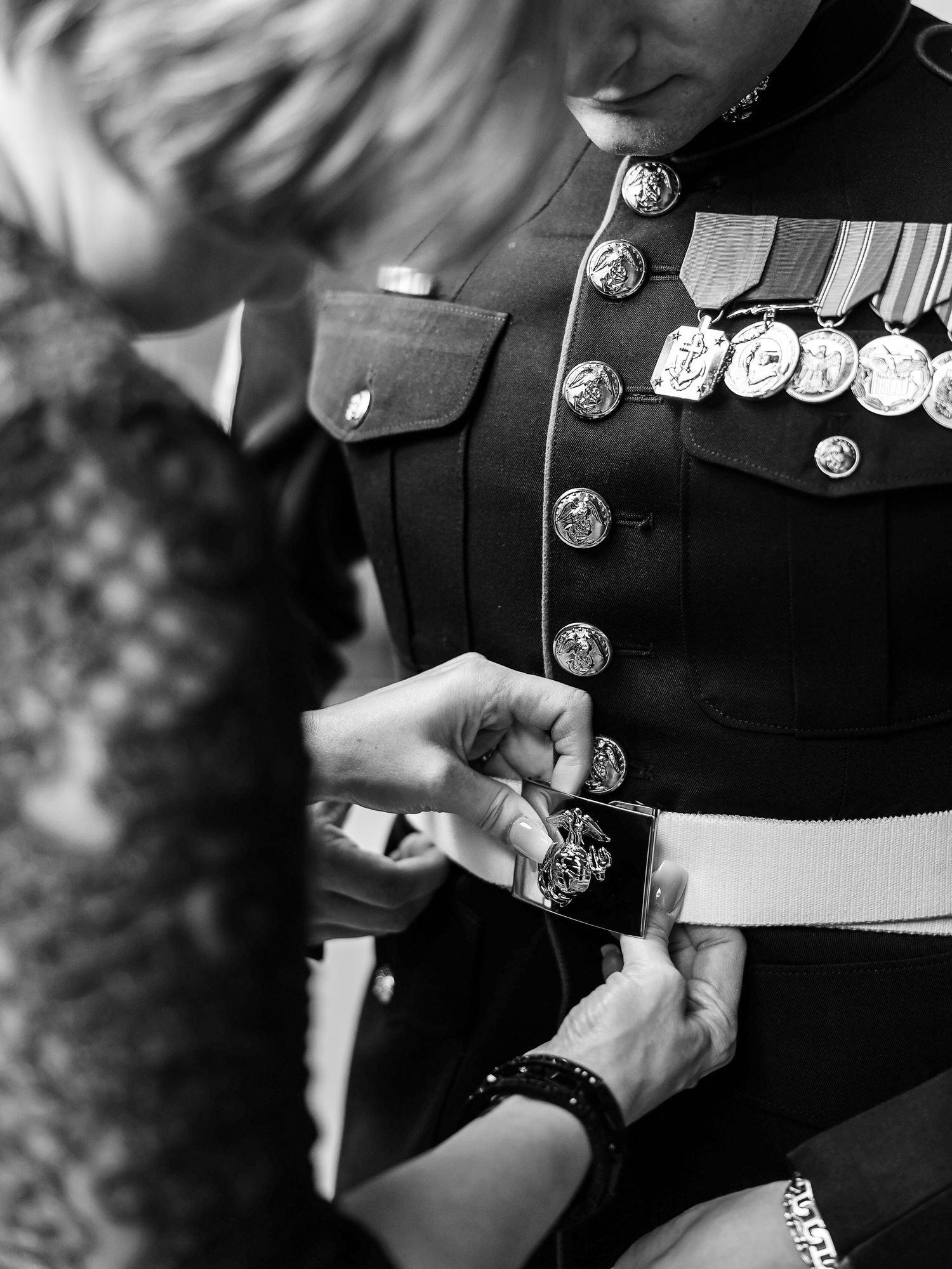 A close-up black and white photo of polished military medals and decorations being adjusted on a formal uniform.