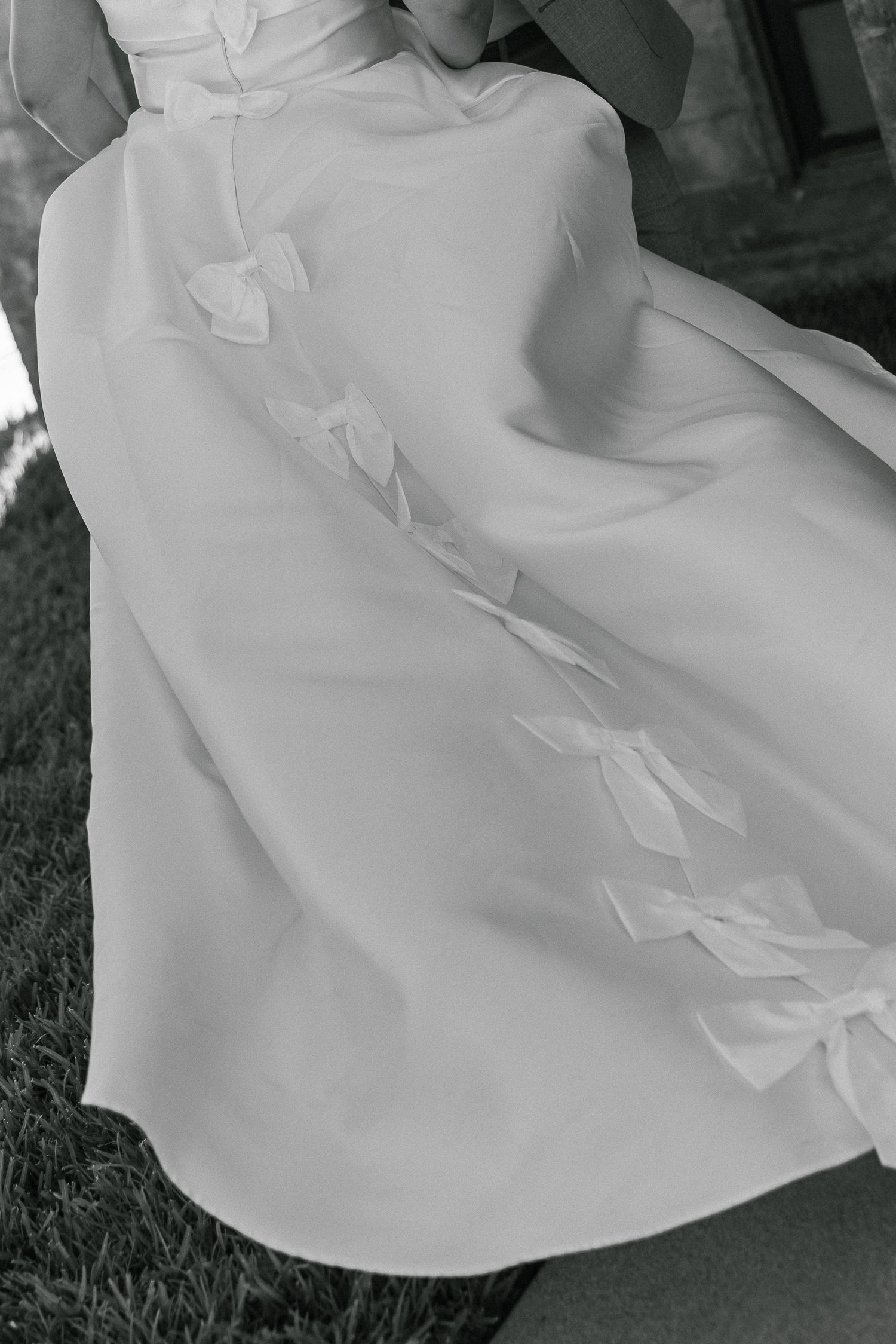 Black and white photo showing detailed fabric texture and bow embellishments on a wedding dress.