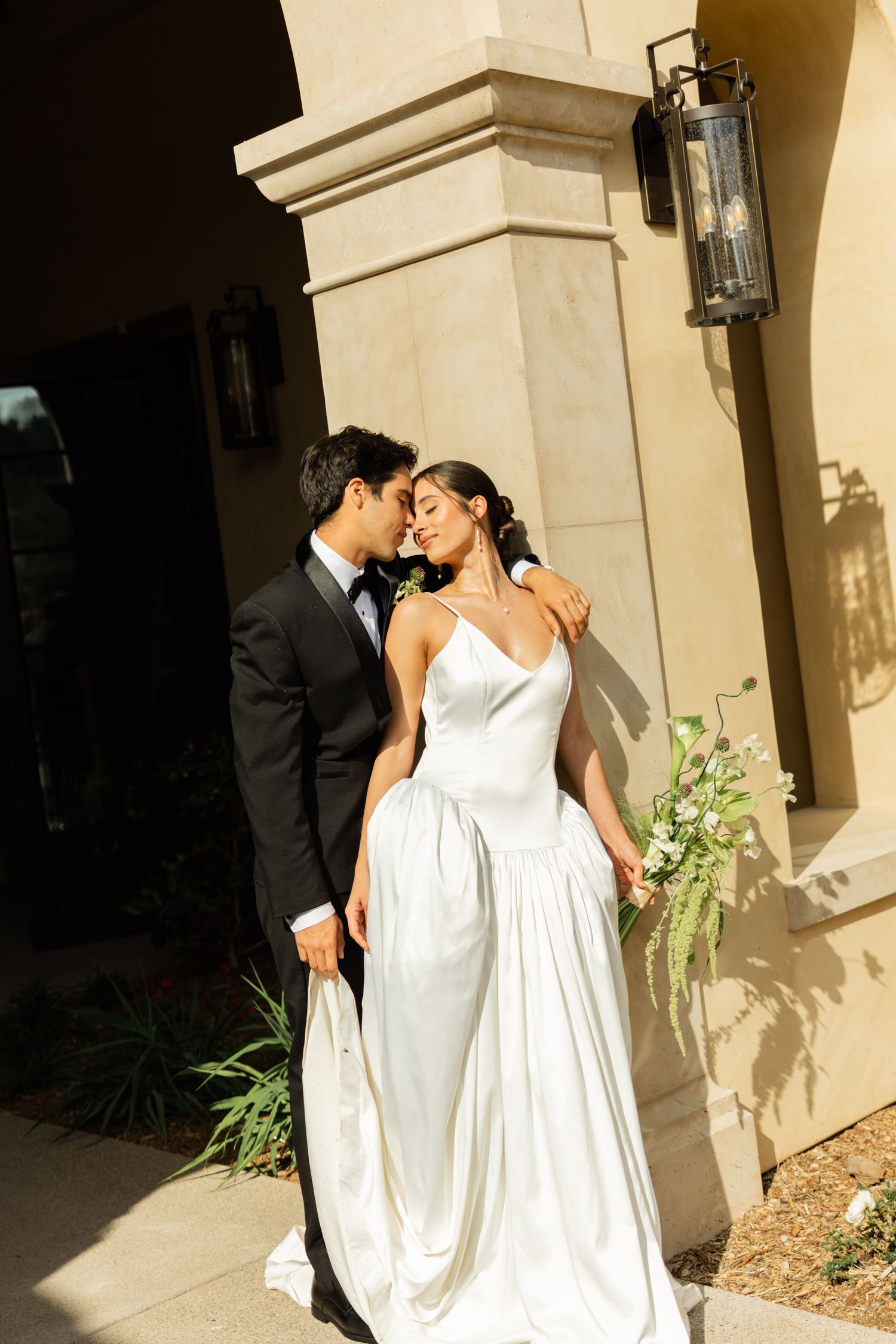 Romantic wedding portrait against beige stone architecture with vintage lantern details.
