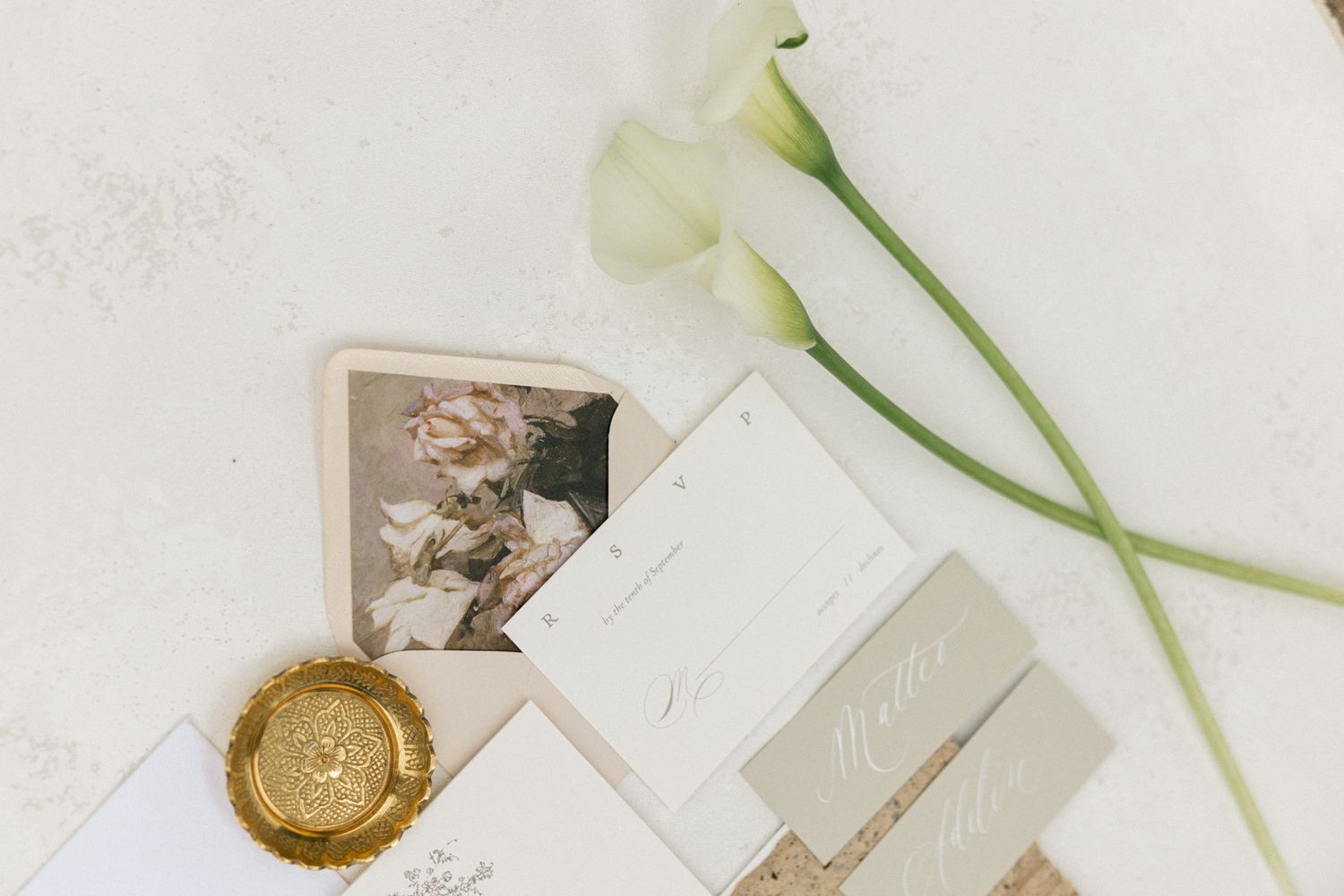 Wedding stationery flatlay with white calla lilies and wax seal on light background.