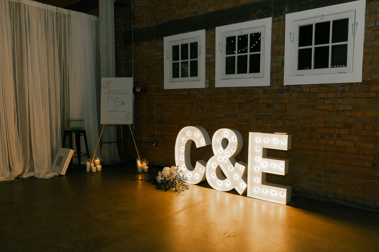 Illuminated marquee letters C&E against exposed brick wall at wedding reception venue.