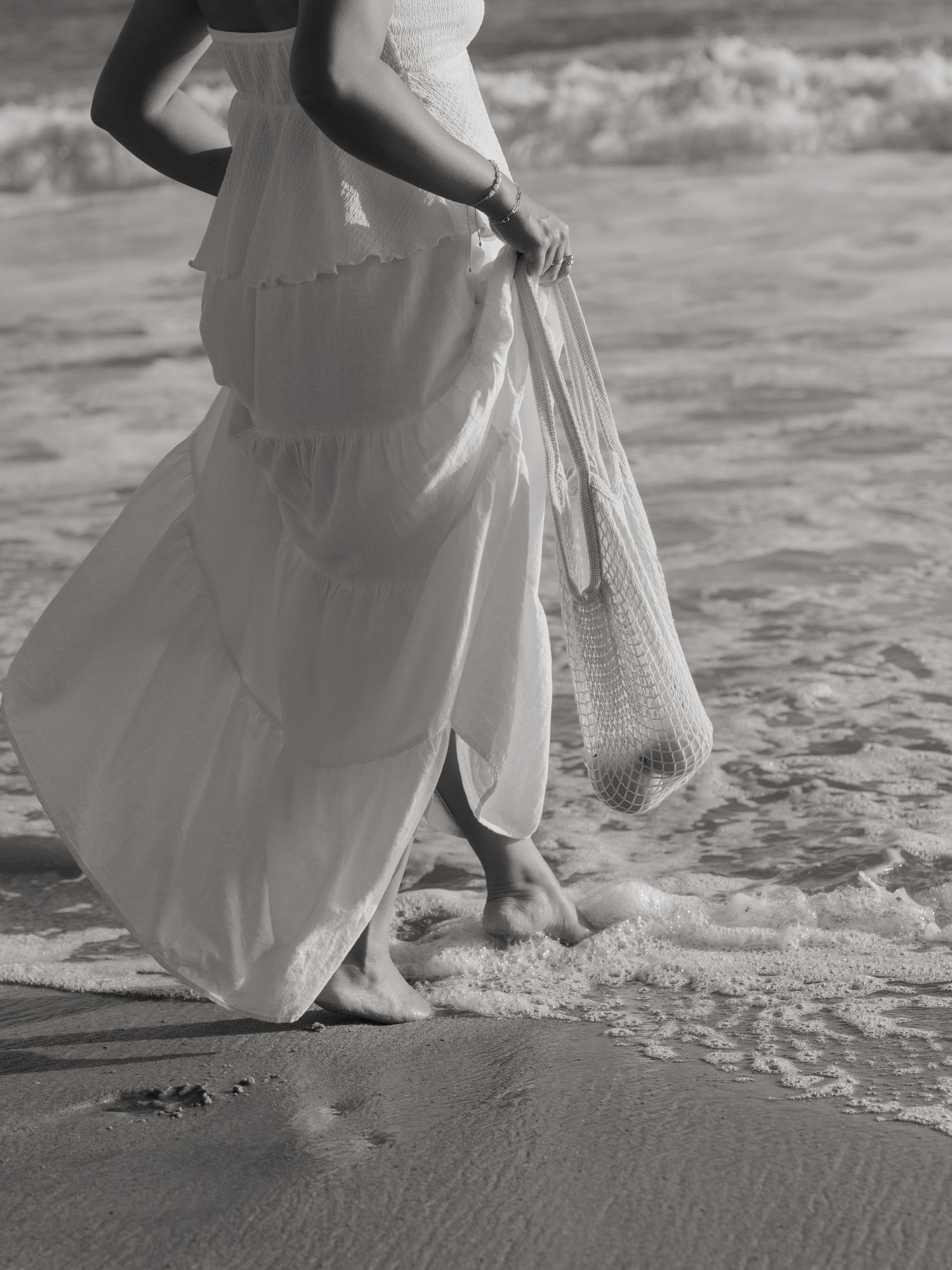 A series of black and white photos showing bare feet walking on a sandy beach with waves and a flowing white dress.