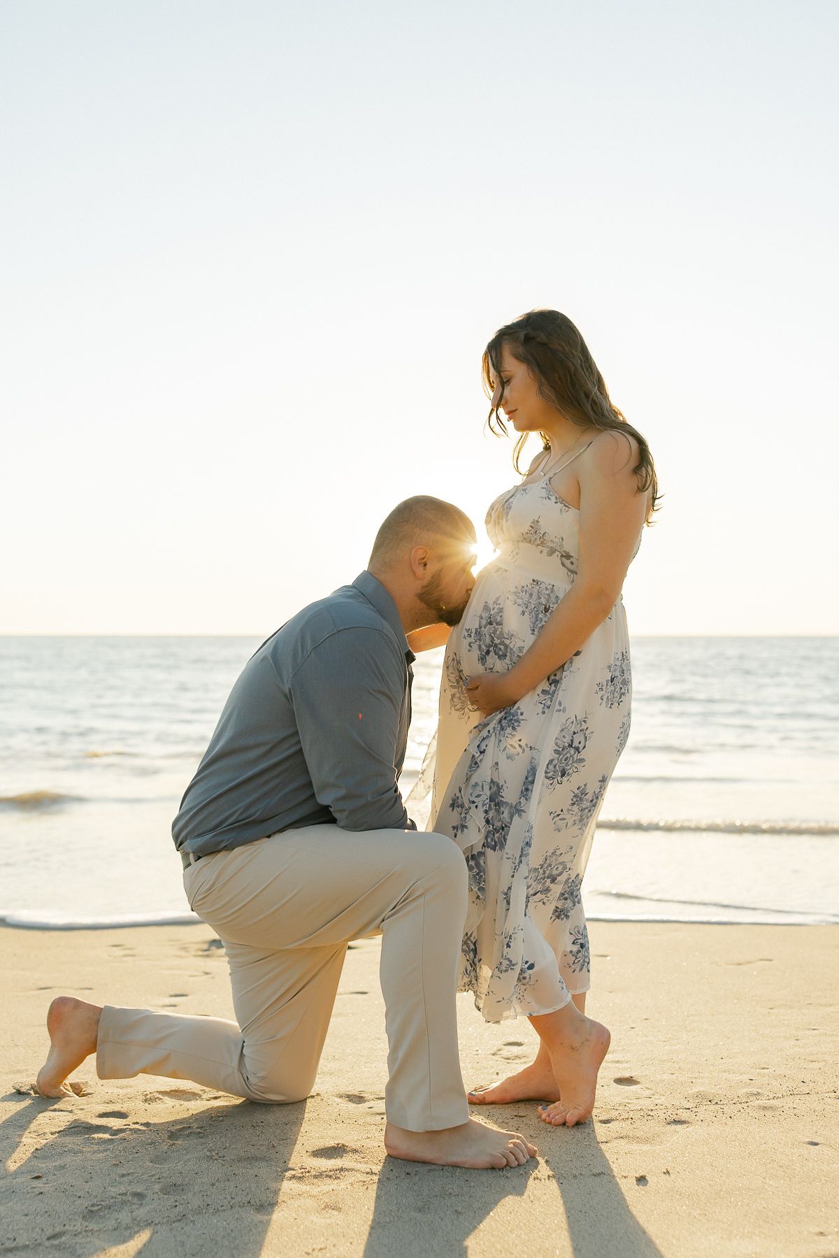Intimate beach maternity photo of a couple sharing a tender moment at sunset.
