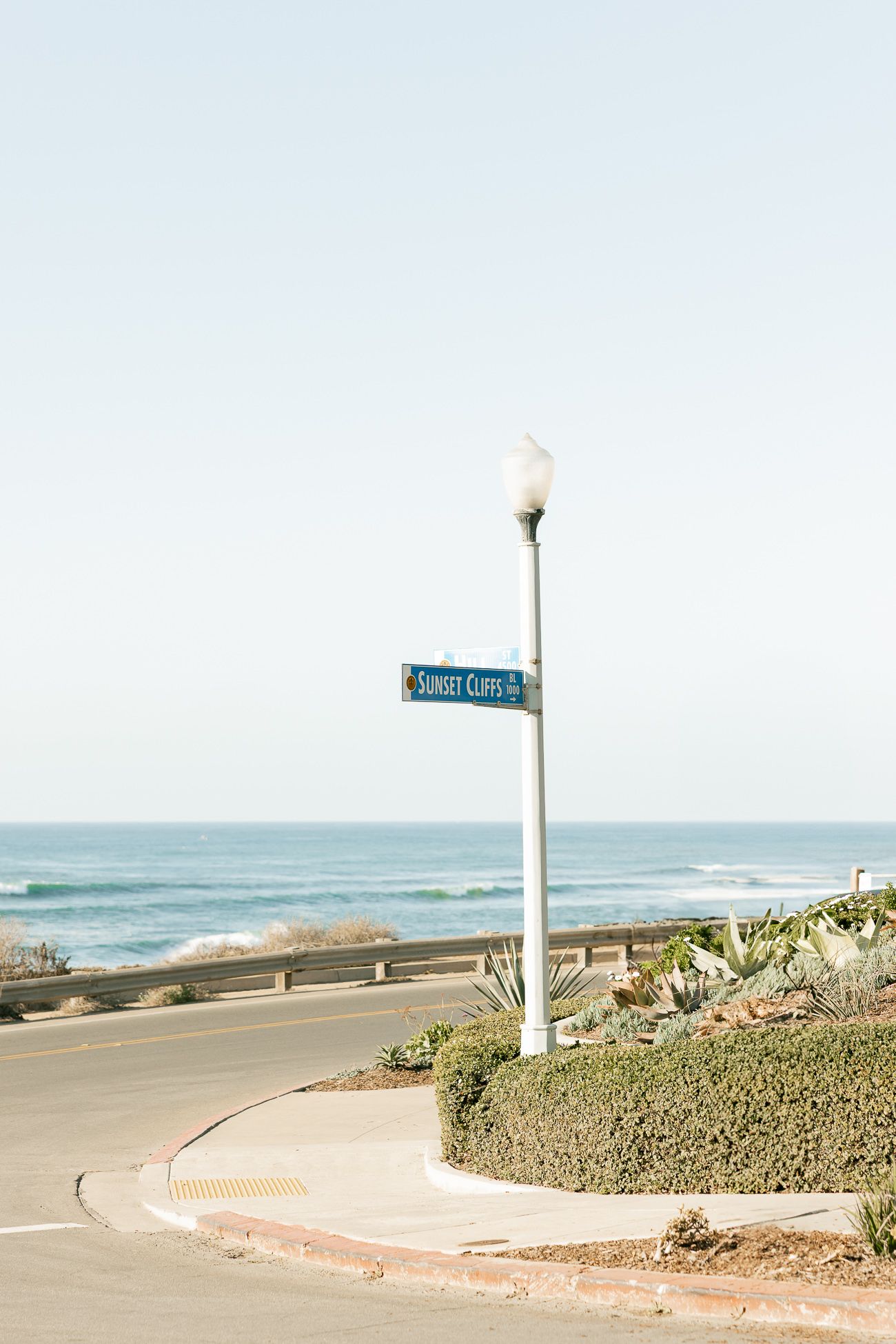 A beachside street corner with Ocean Cliff street sign and vintage lamp post overlooking the Pacific Ocean.