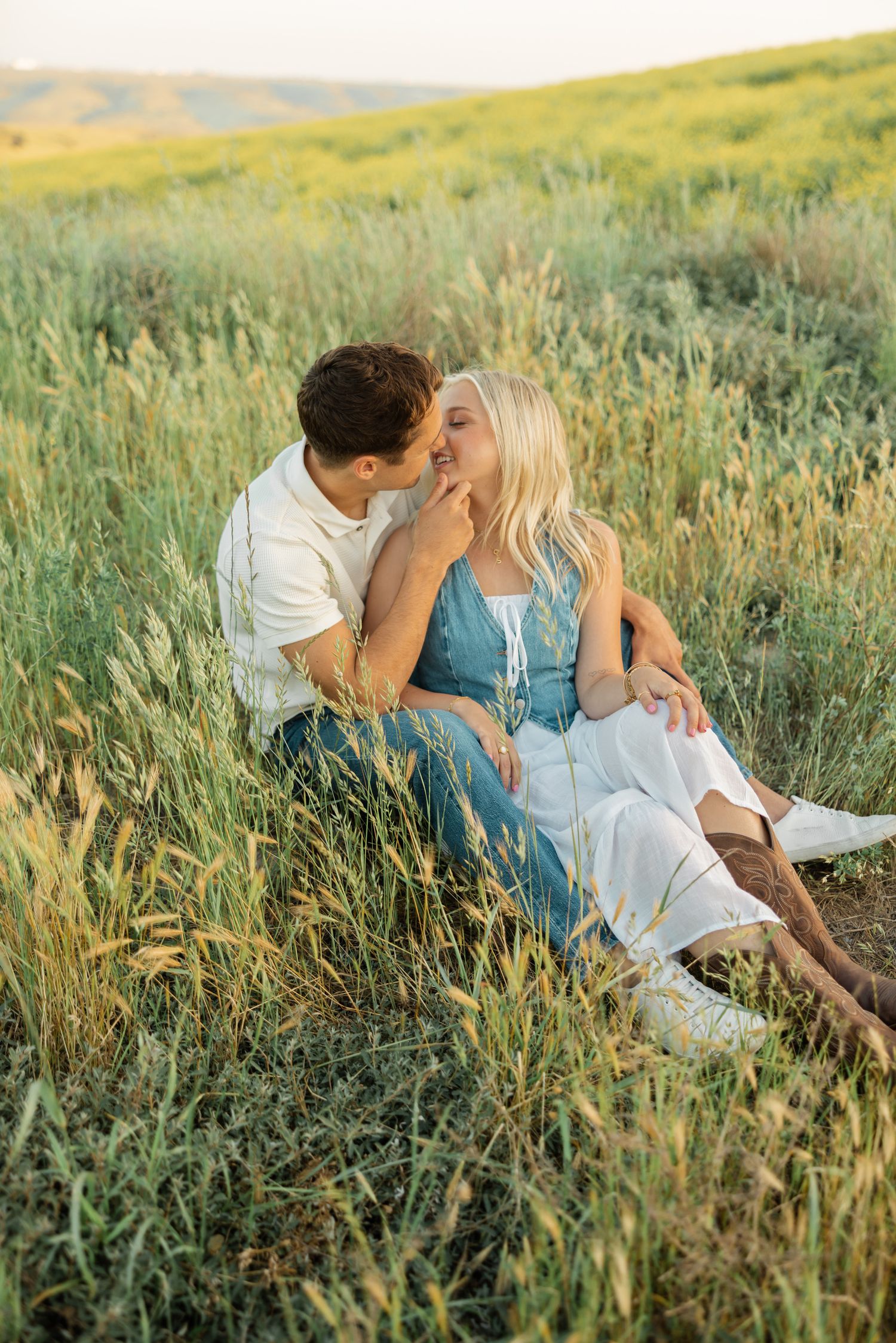 A romantic couple shares tender moments together while lying in a sunlit meadow of tall grass during golden hour.