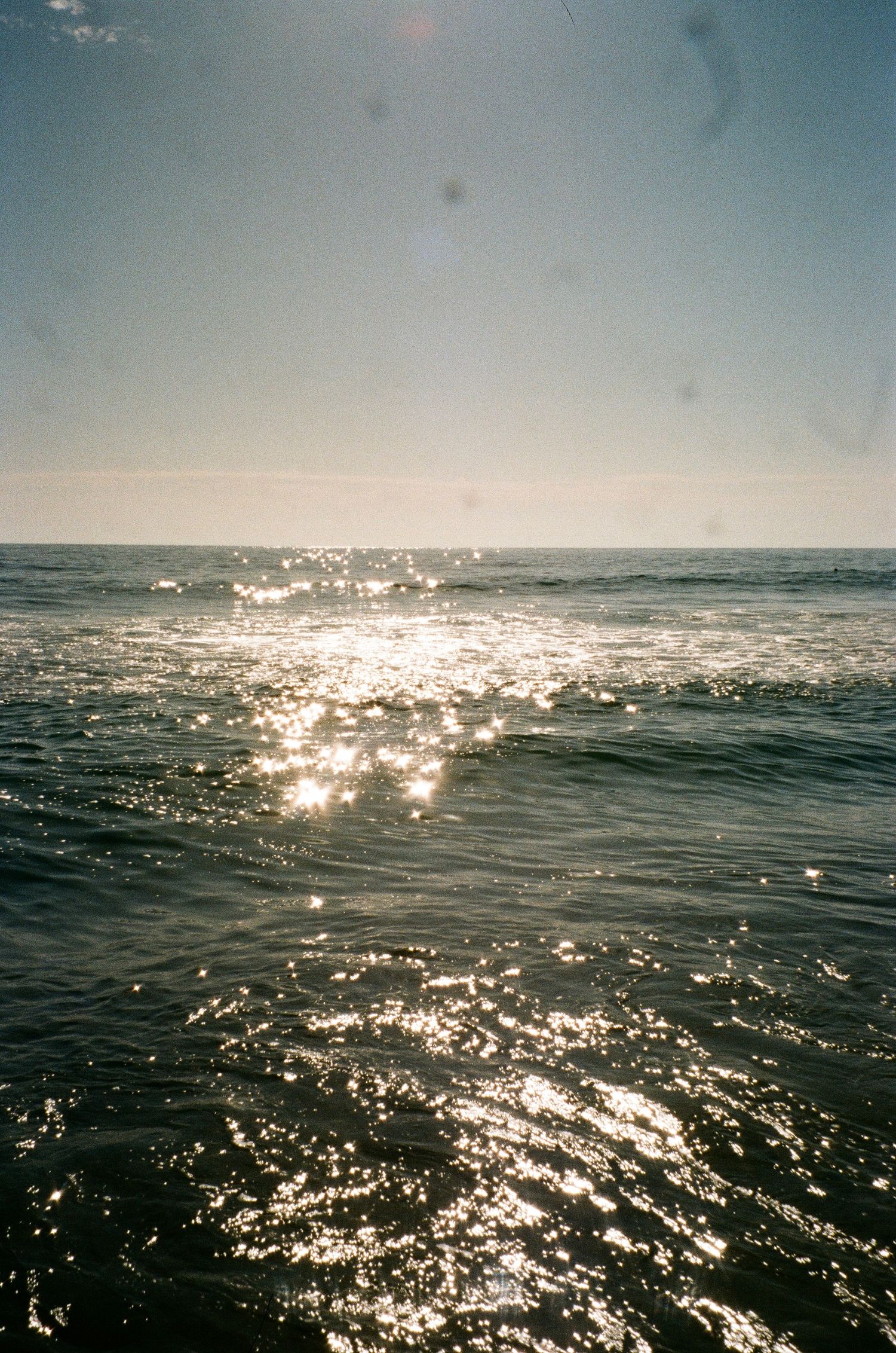 Sunlight sparkles across ocean waves under soft blue sky.