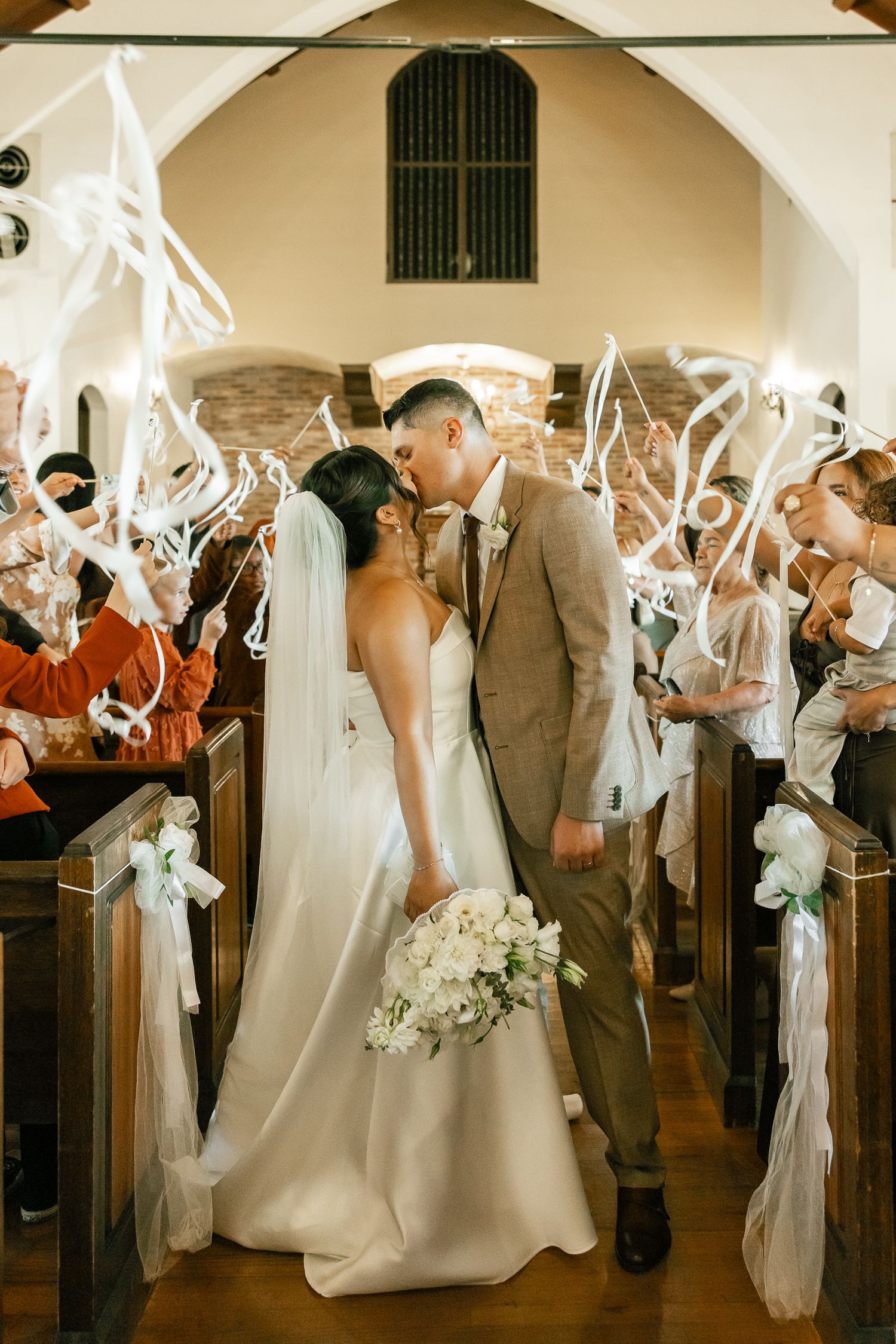A joyful wedding couple shares a kiss in a church aisle while guests wave sparklers during their ceremony exit.