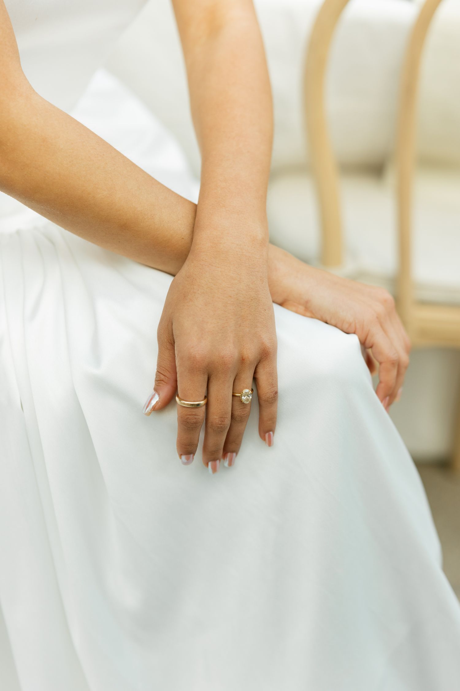 A bride's hand rests on her white wedding dress, showing off an elegant engagement ring.