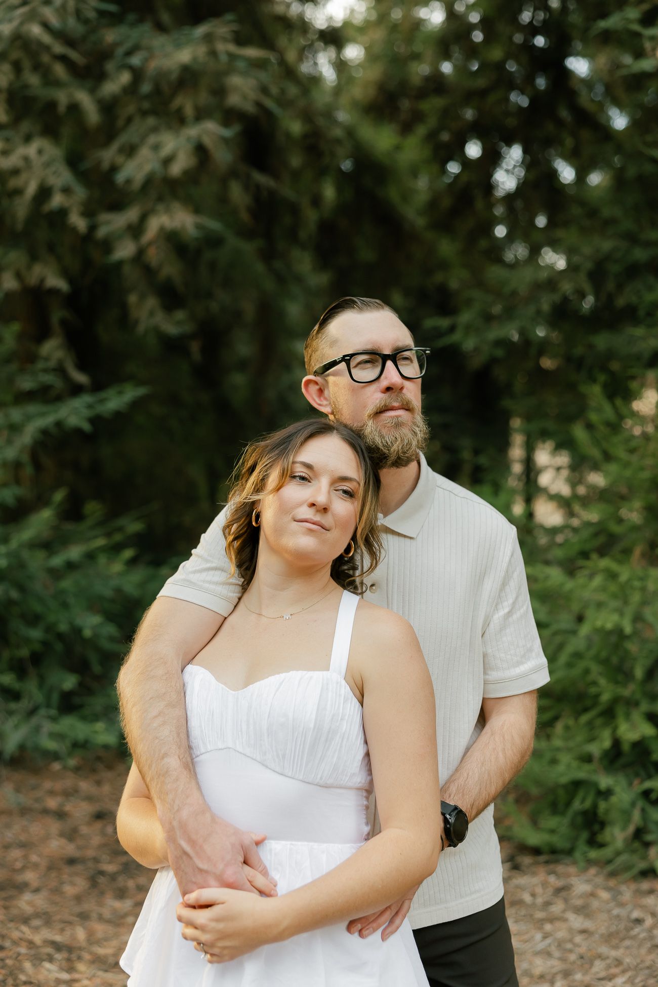 A couple embraces outdoors in a wooded setting, with green foliage in the background.