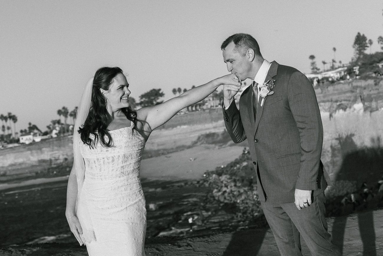 Black and white photo of newlyweds sharing a playful moment outdoors.