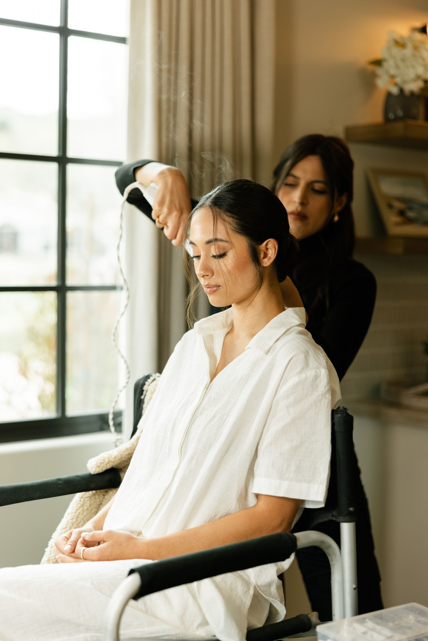 A massage therapist in white uniform performs therapeutic treatment in a serene spa setting near large windows.