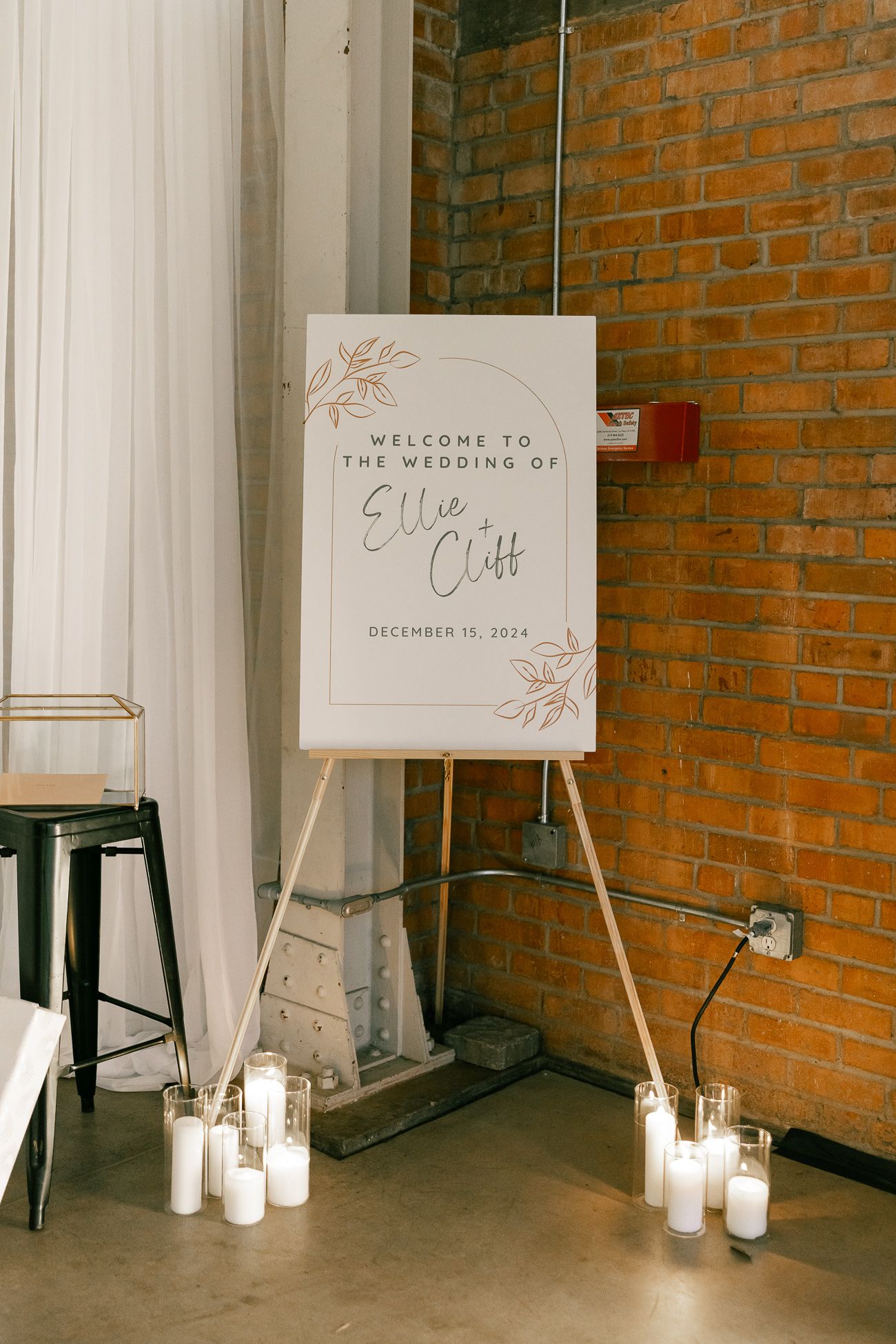 Wedding welcome sign on an easel with white candles displayed against exposed brick wall.