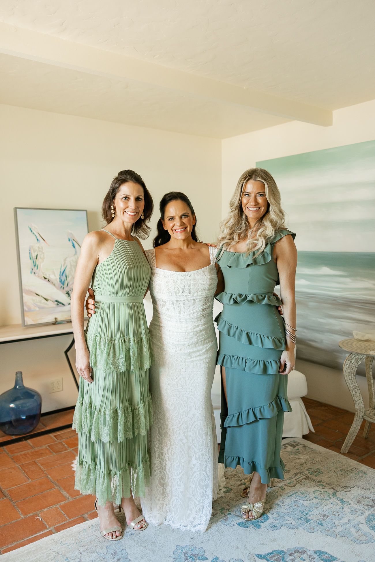 Wedding party posing in coordinated mint and teal tiered dresses against a coastal artwork.