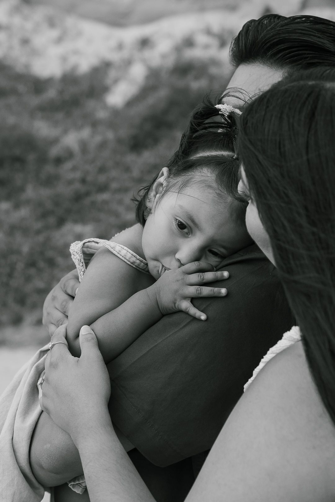 A tender black and white portrait of a parent embracing and comforting a small child against a blurred outdoor background.