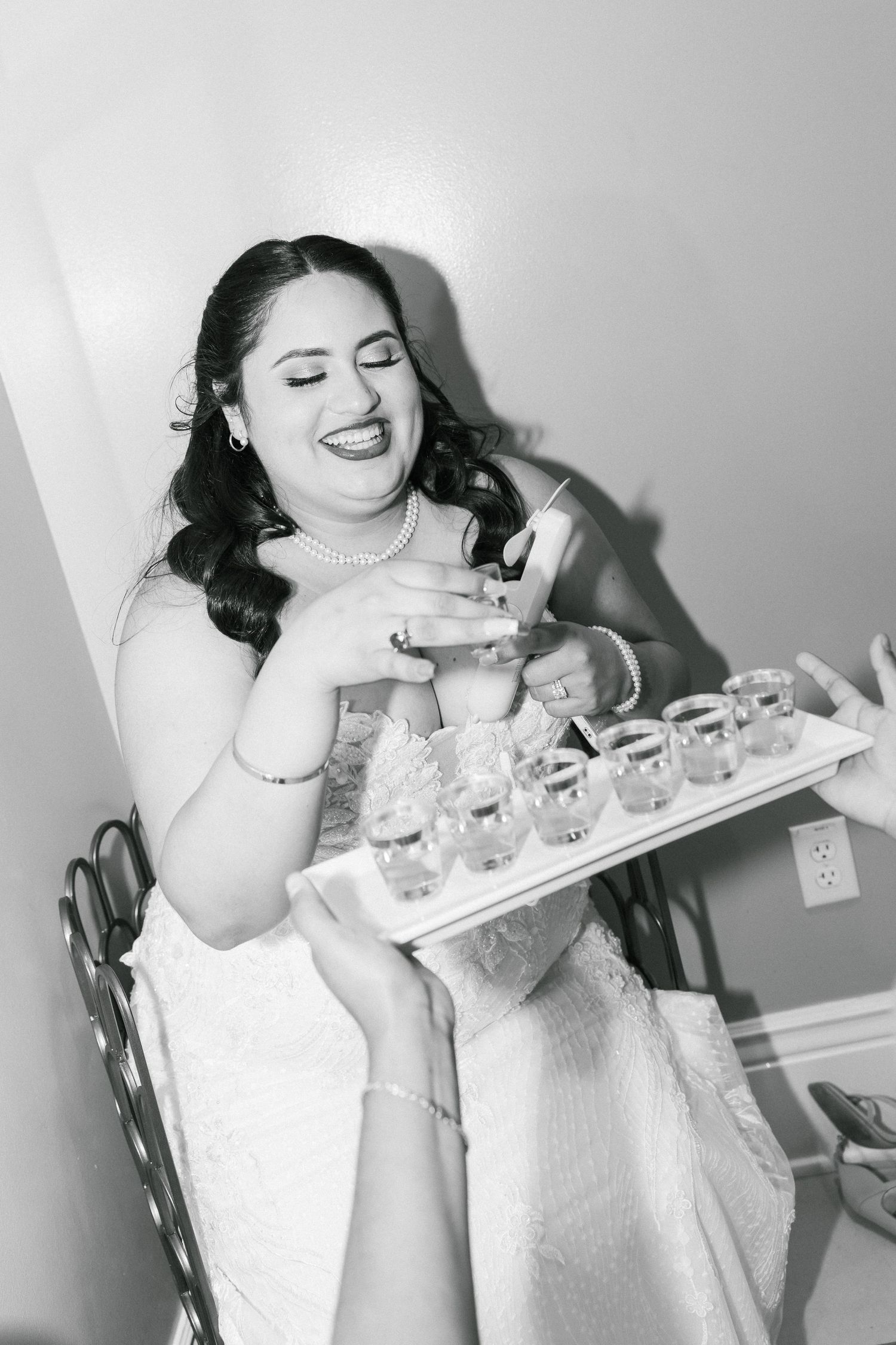 A joyful bride in a white dress laughs while holding a tray of drinks during a wedding celebration.