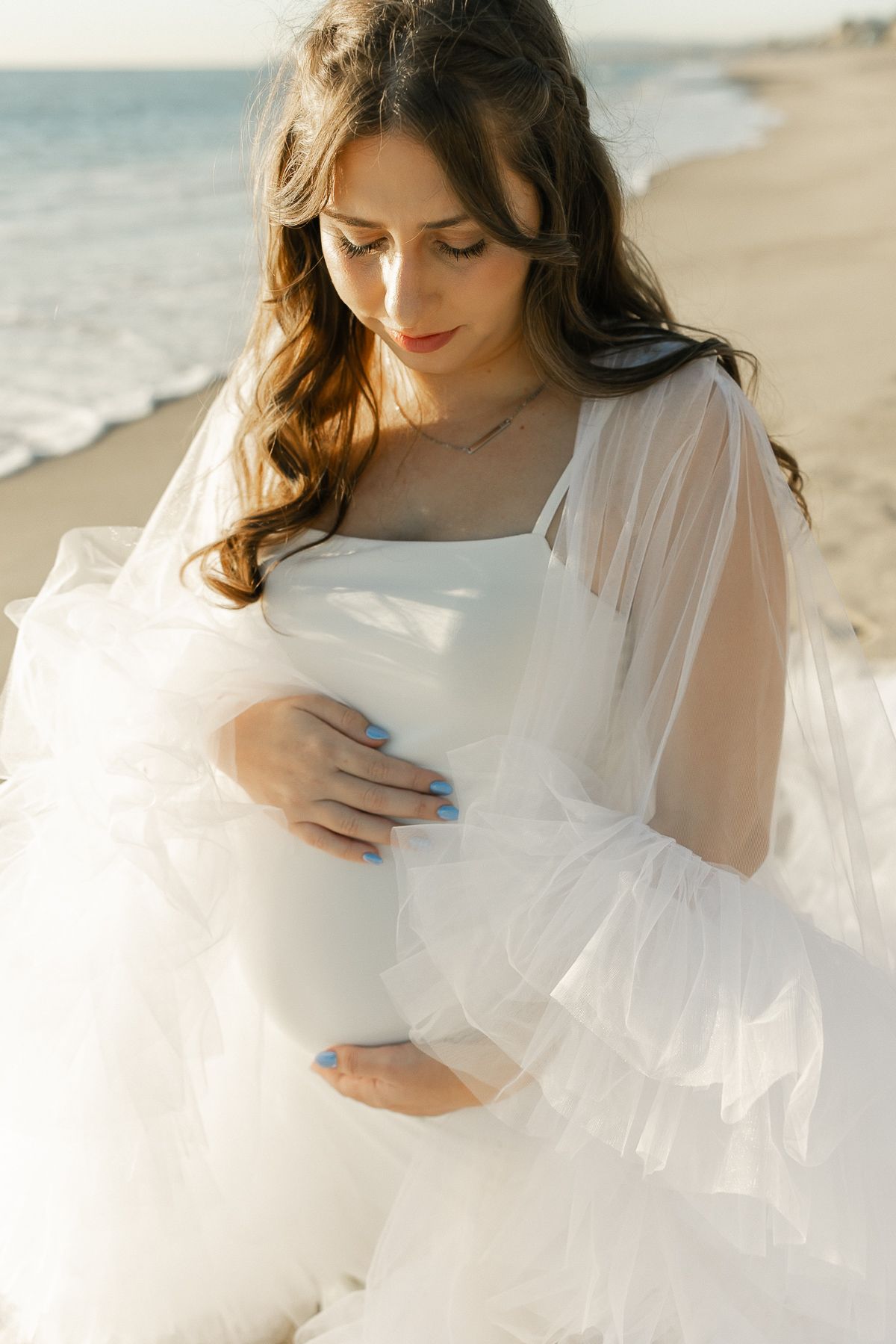 Ethereal beach photoshoot featuring flowing white dress against golden sunlight.