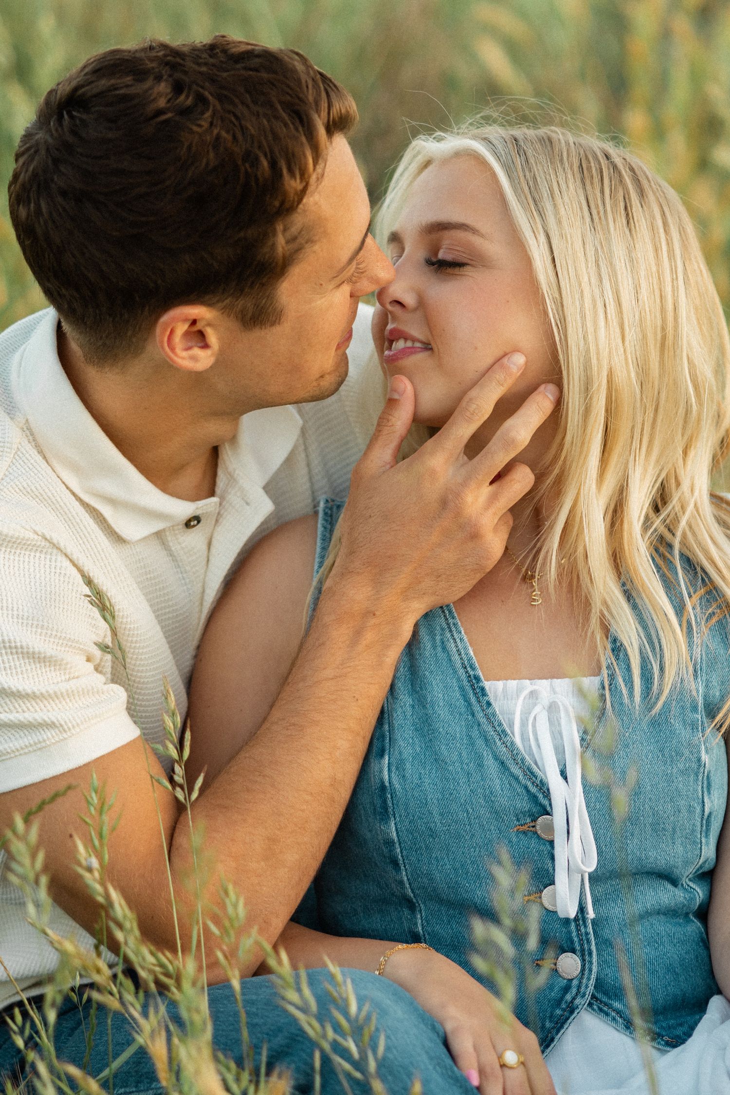 A romantic couple shares tender moments in tall grass wearing white and blue outfits in a series of intimate photos.