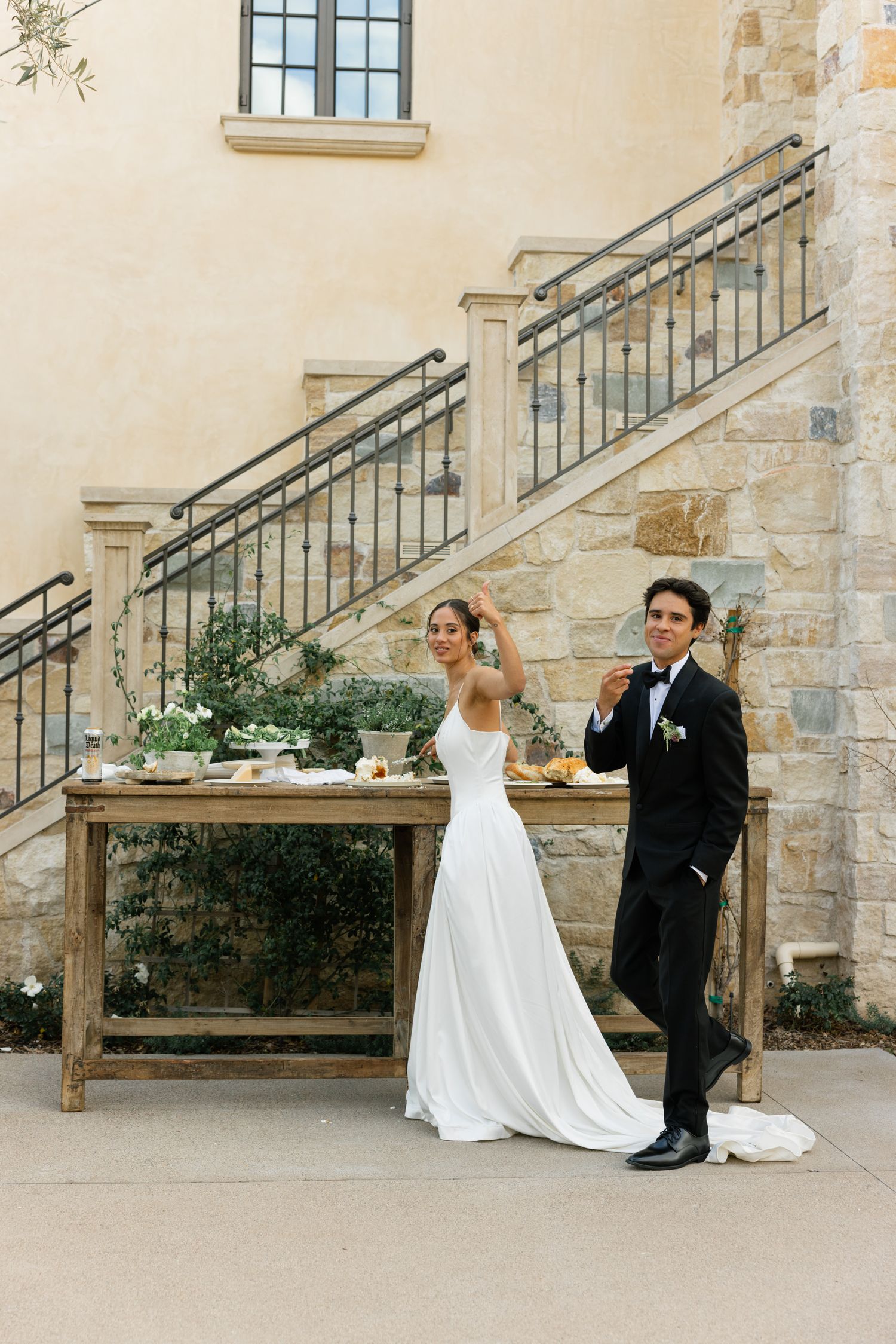 A couple celebrates during their wedding at a stone staircase with a rustic wooden table and elegant decor.