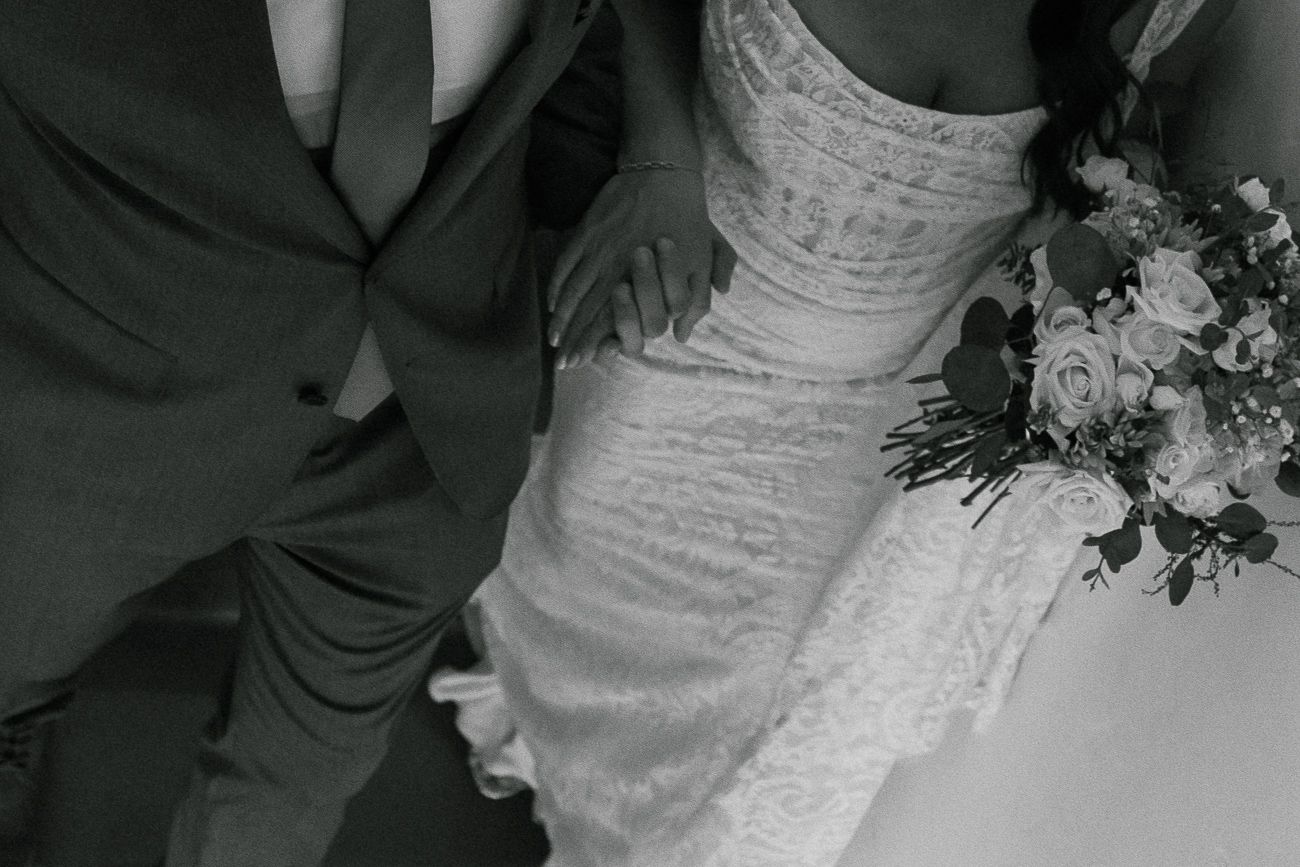 A black and white close-up shot of the intricate details on a wedding dress with a bouquet.