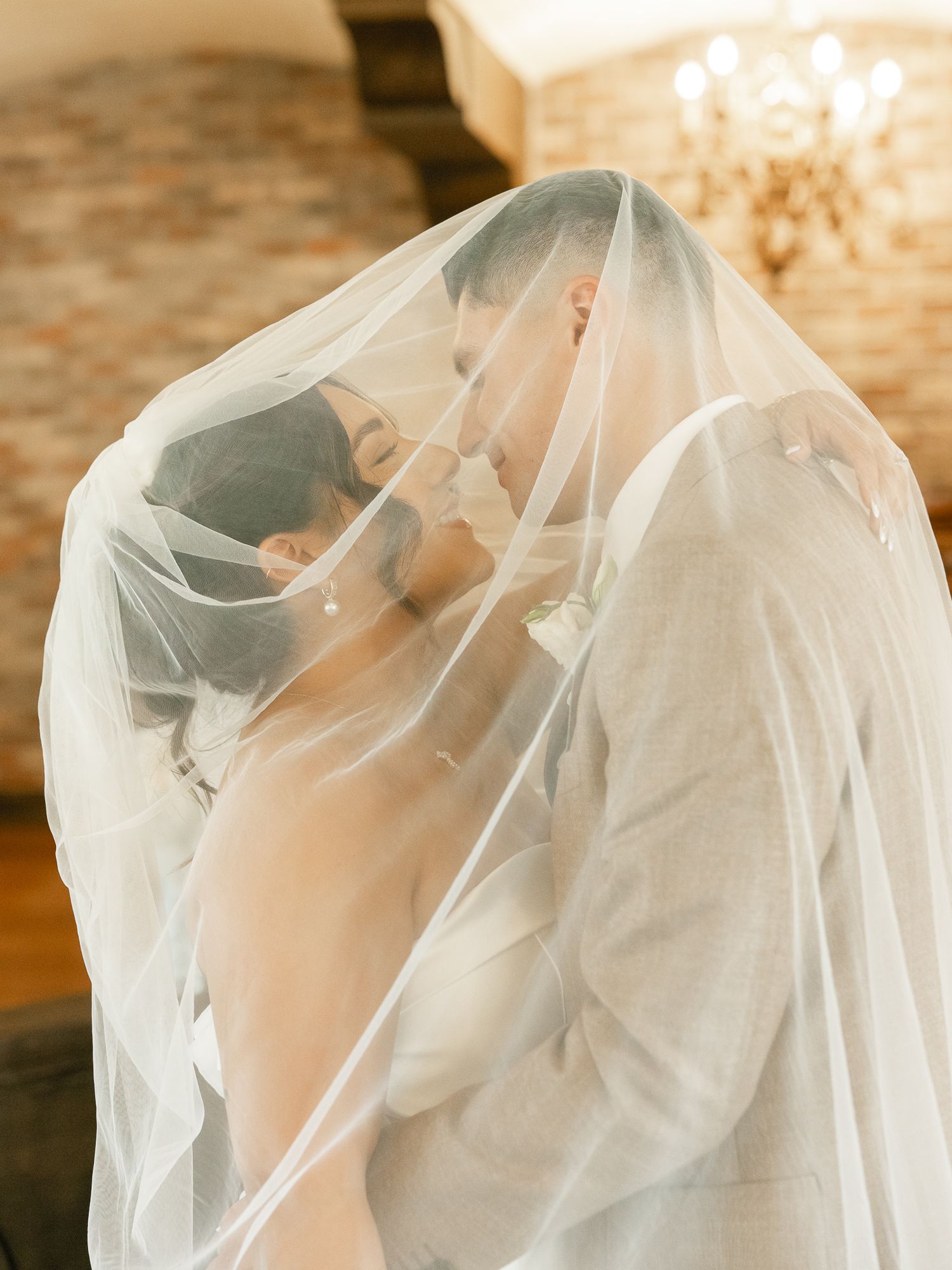A bride and groom share an intimate moment under a delicate white veil during their wedding ceremony.