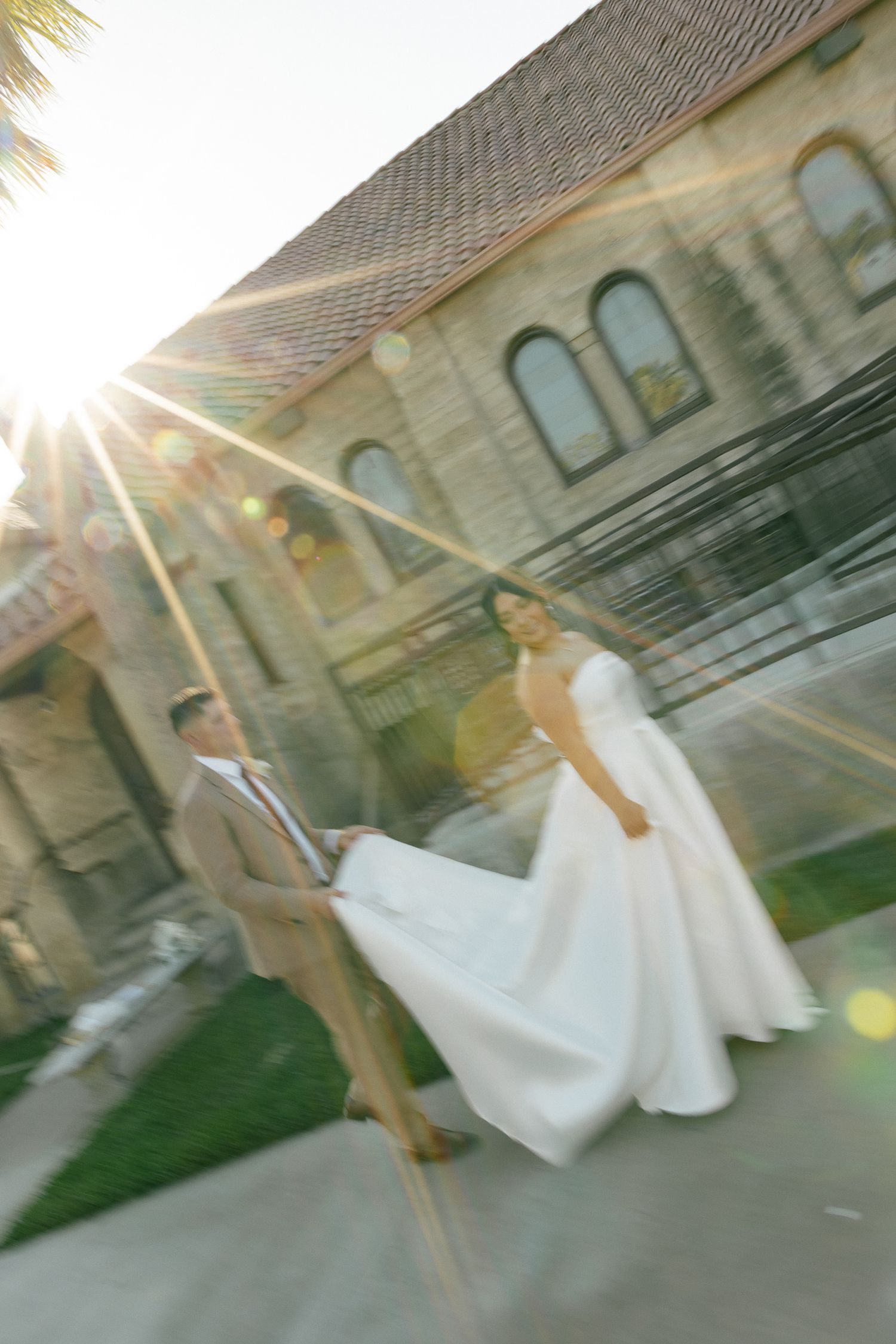 A sunlit artistic wedding photo outside a stone church with lens flare and motion blur effects.