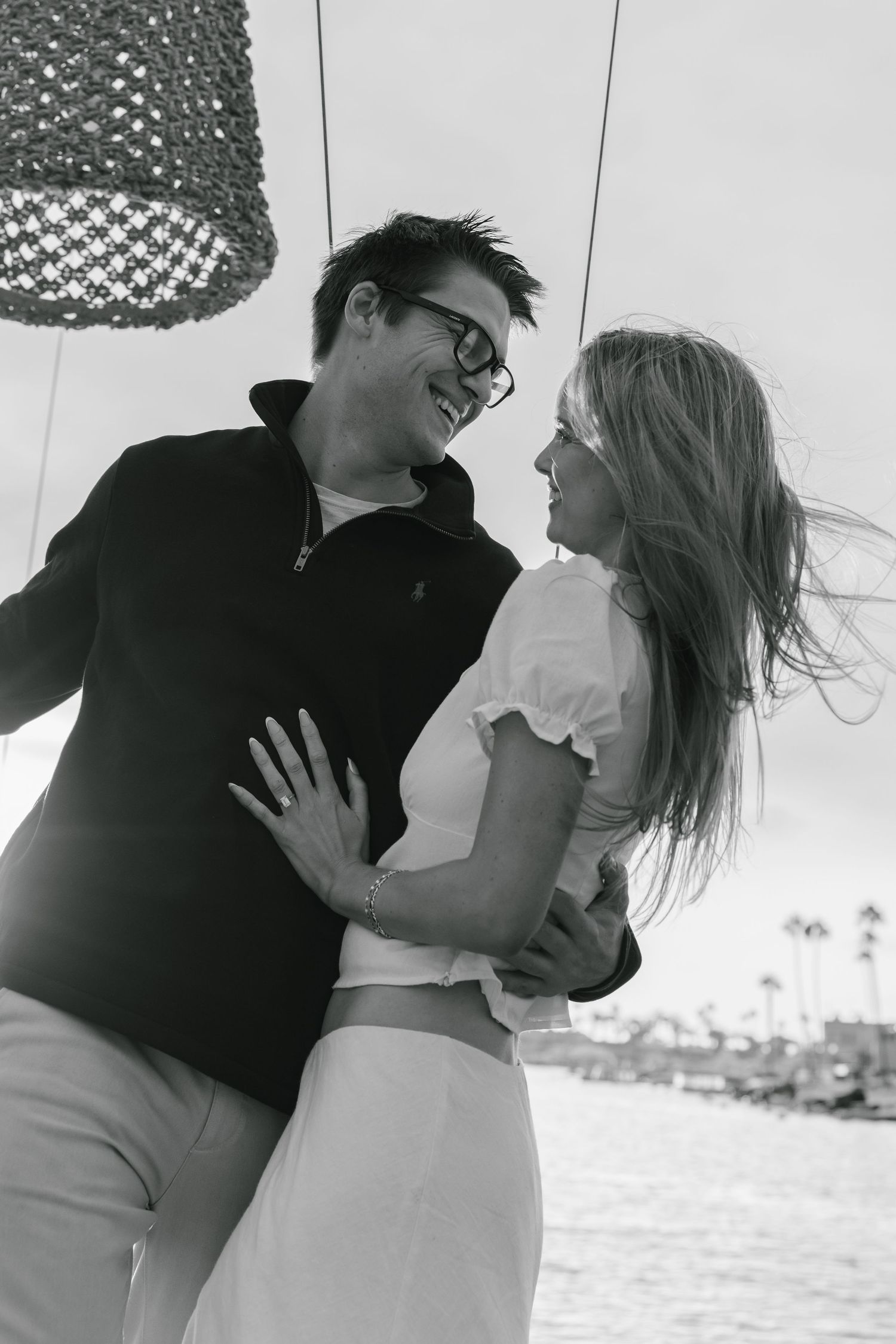 A black and white photo of a couple sharing a playful moment under a hanging light fixture.