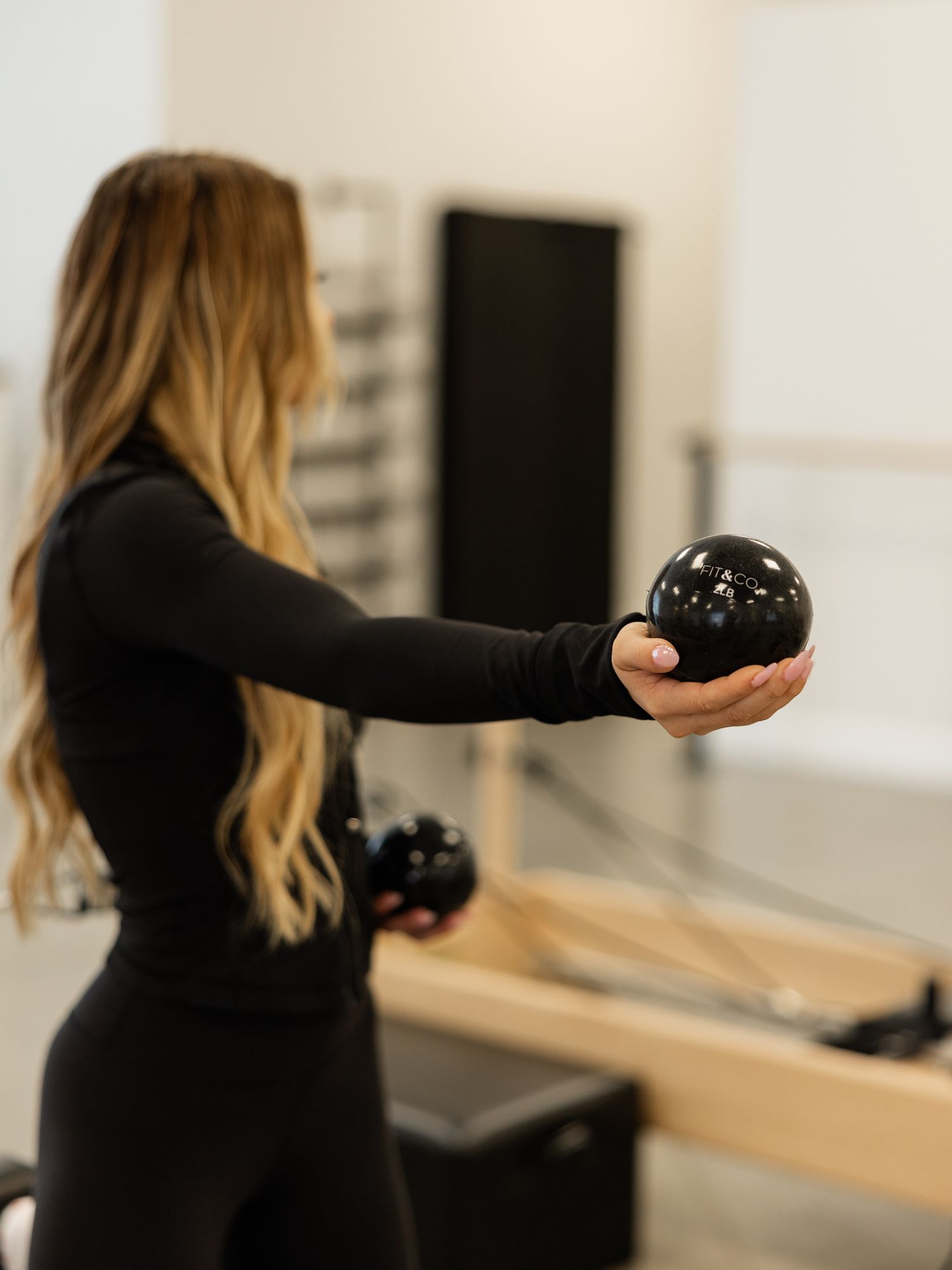 Instructor demonstrating arm movements with a weighted ball during a Pilates session.