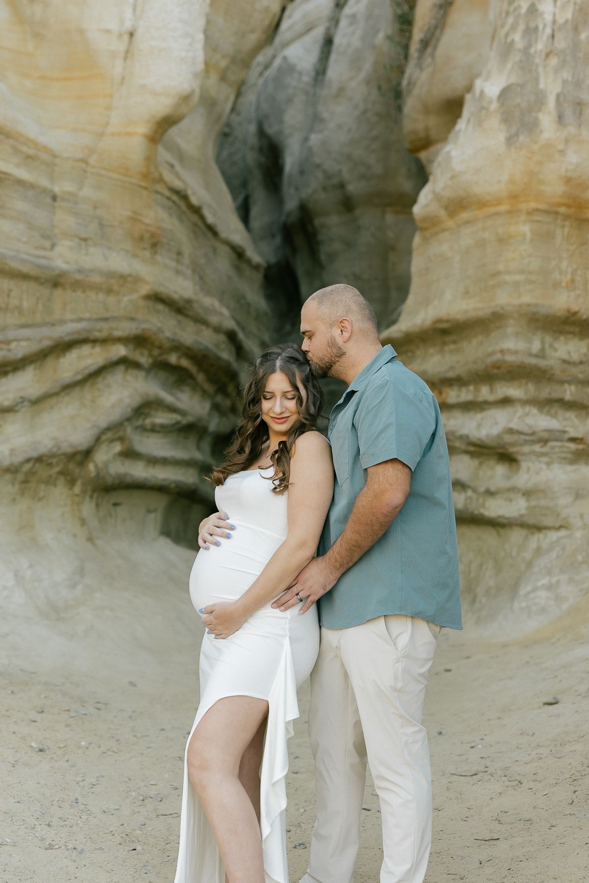 Maternity photo session against dramatic rock formations with couple in white and blue outfits.
