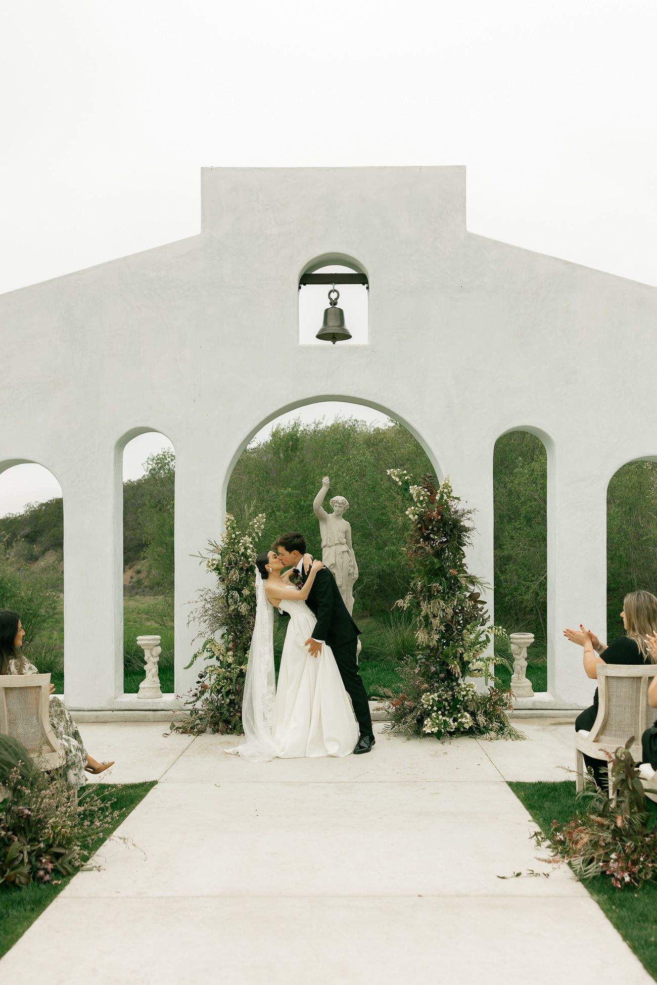 A panoramic view of a white arched colonnade with greenery and flowers in an elegant outdoor wedding setting.