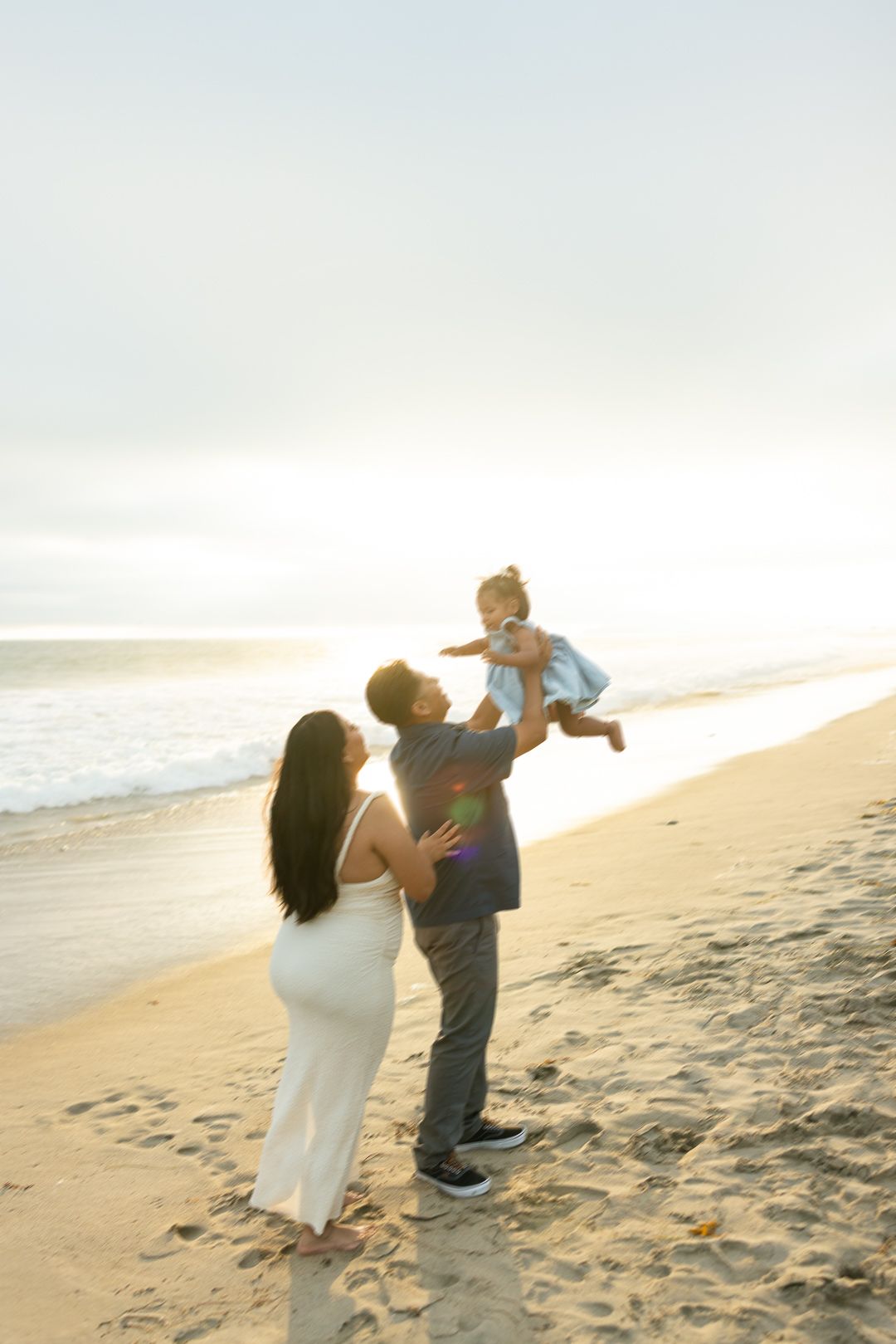 Family playing and lifting child on sunny beach at sunset creating joyful moments together.