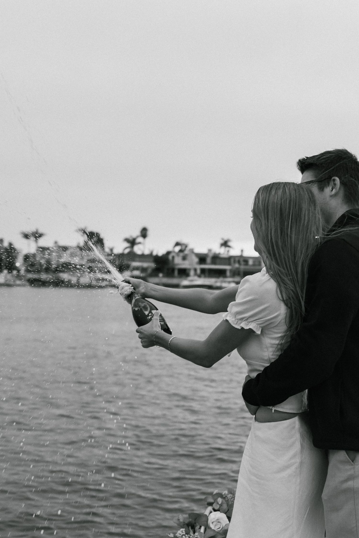 A couple practicing target shooting with handguns at an outdoor waterfront range in black and white.