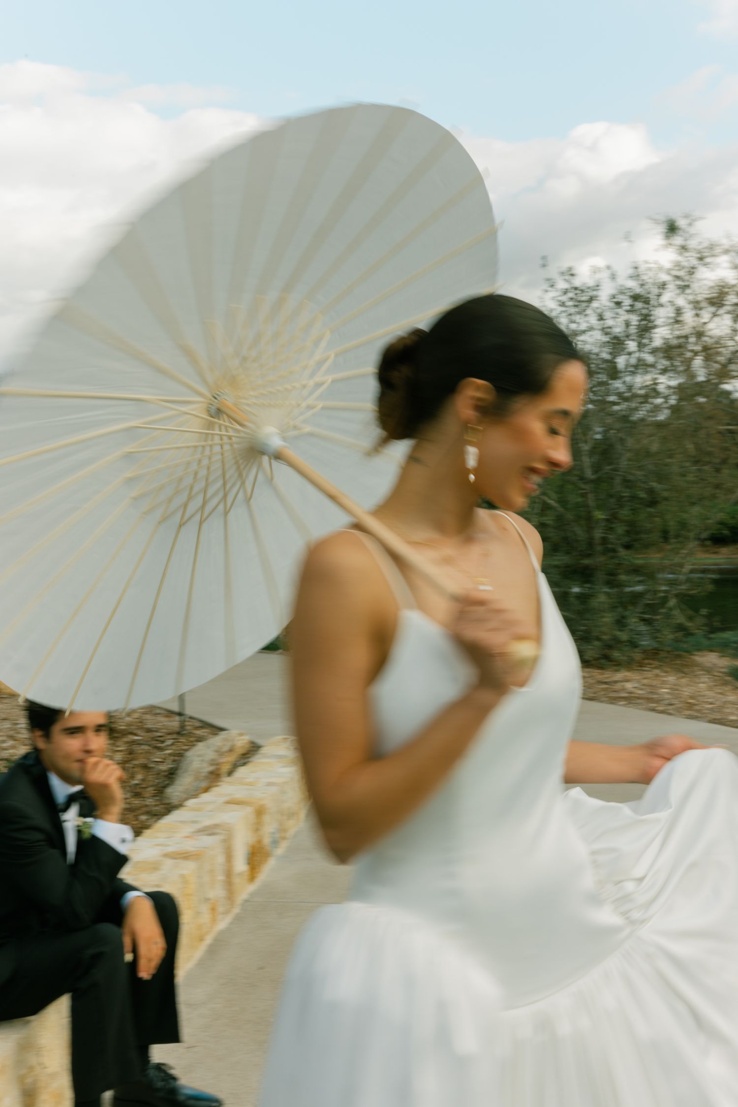 A bride in a flowing white dress twirls beneath a delicate paper parasol on her wedding day.