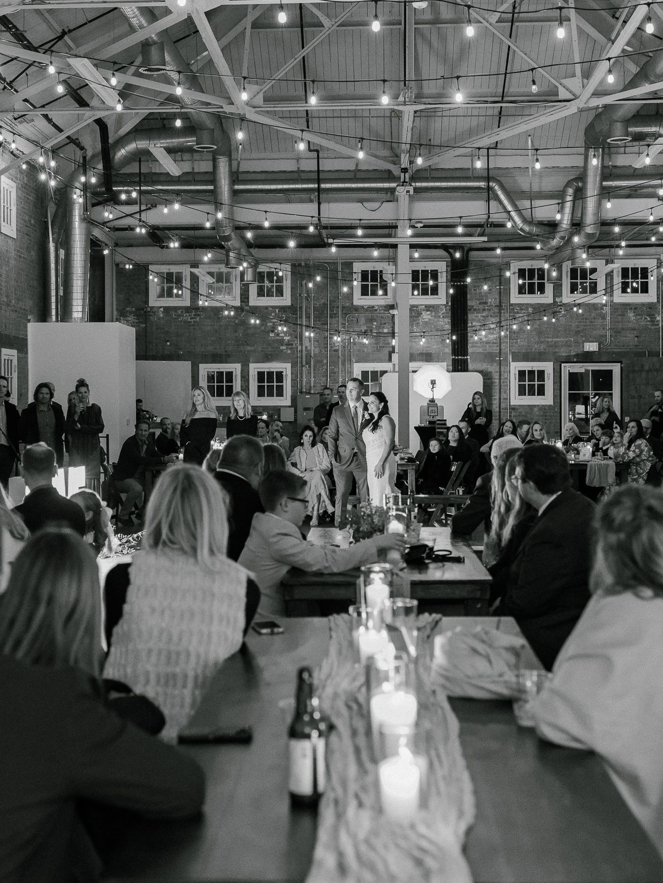 Black and white photos show guests seated at round tables during an elegant indoor wedding reception with string lights overhead.
