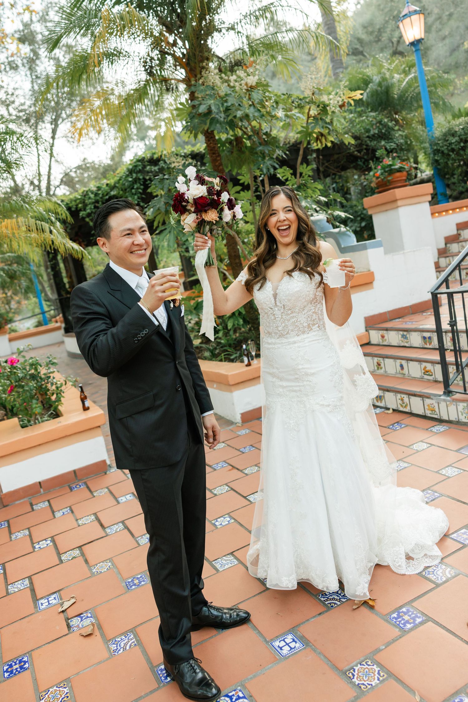 A couple shares a joyful moment dancing together on a Spanish-style tiled patio with decorative railings and lush greenery.
