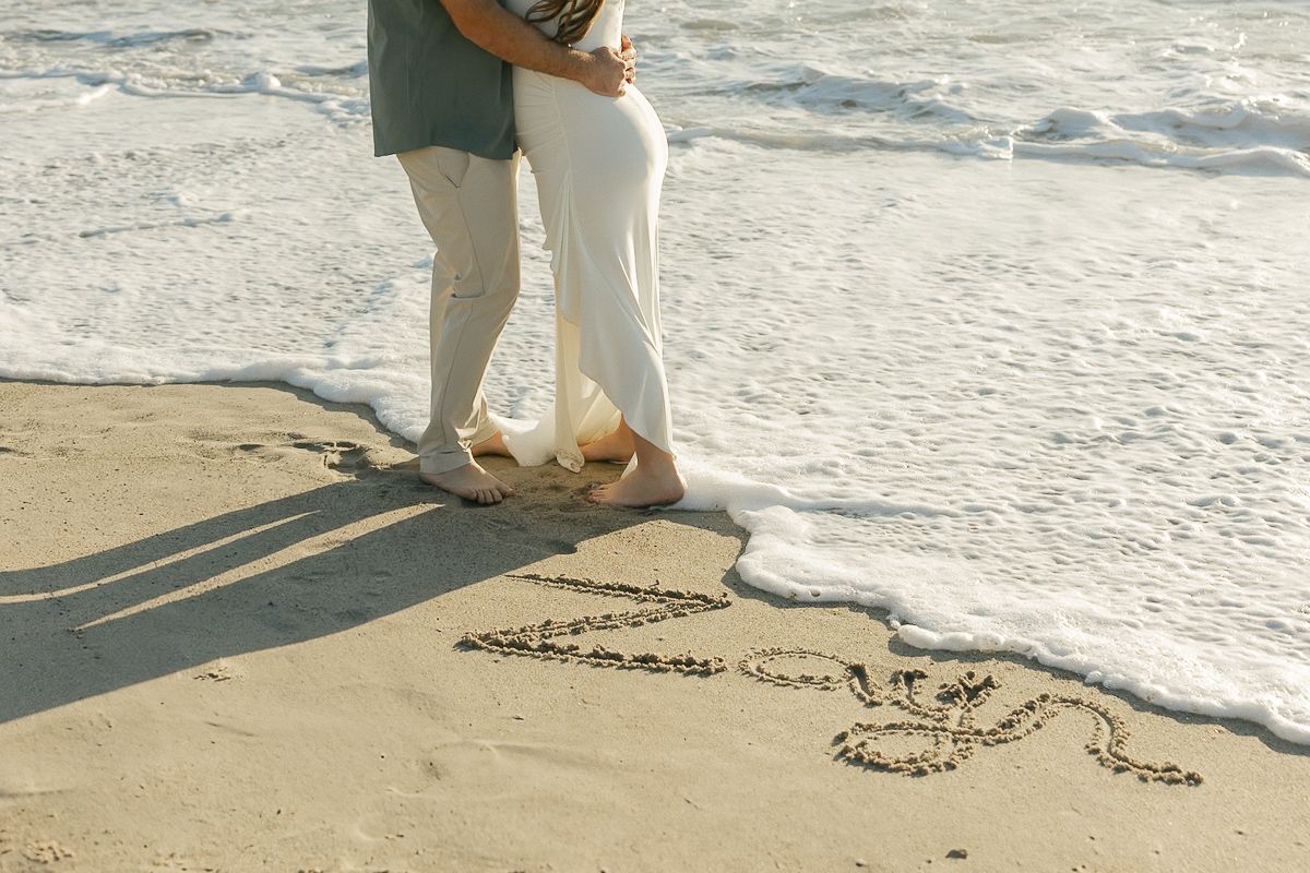 A couple writes a message in the sand on a peaceful beach during golden hour.