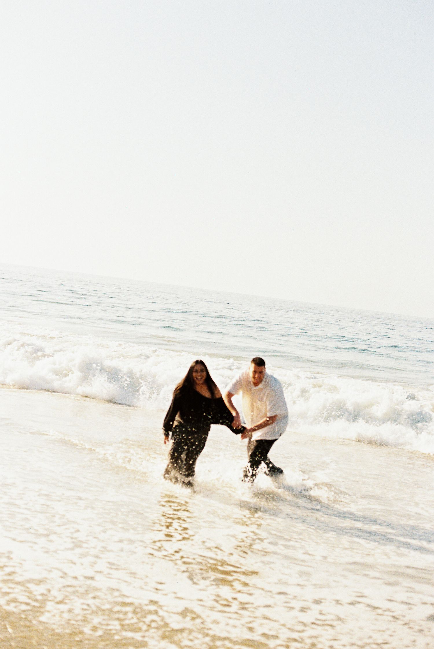 Two people playing and splashing in the ocean waves during a bright sunny day at the beach.