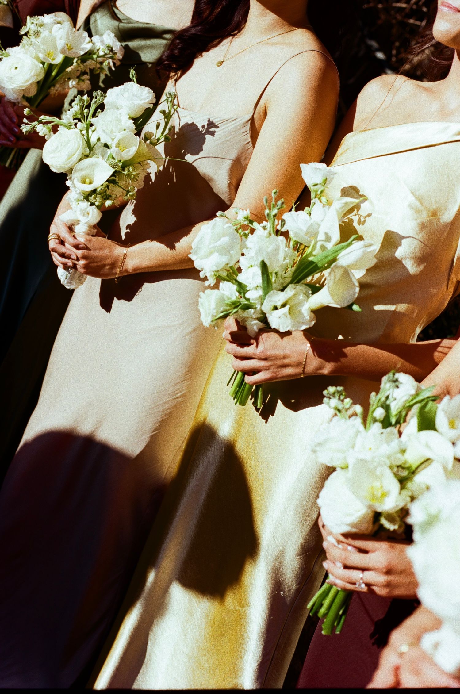 Bridesmaids in elegant white dresses stand in line holding matching white and green floral bouquets at a wedding ceremony.