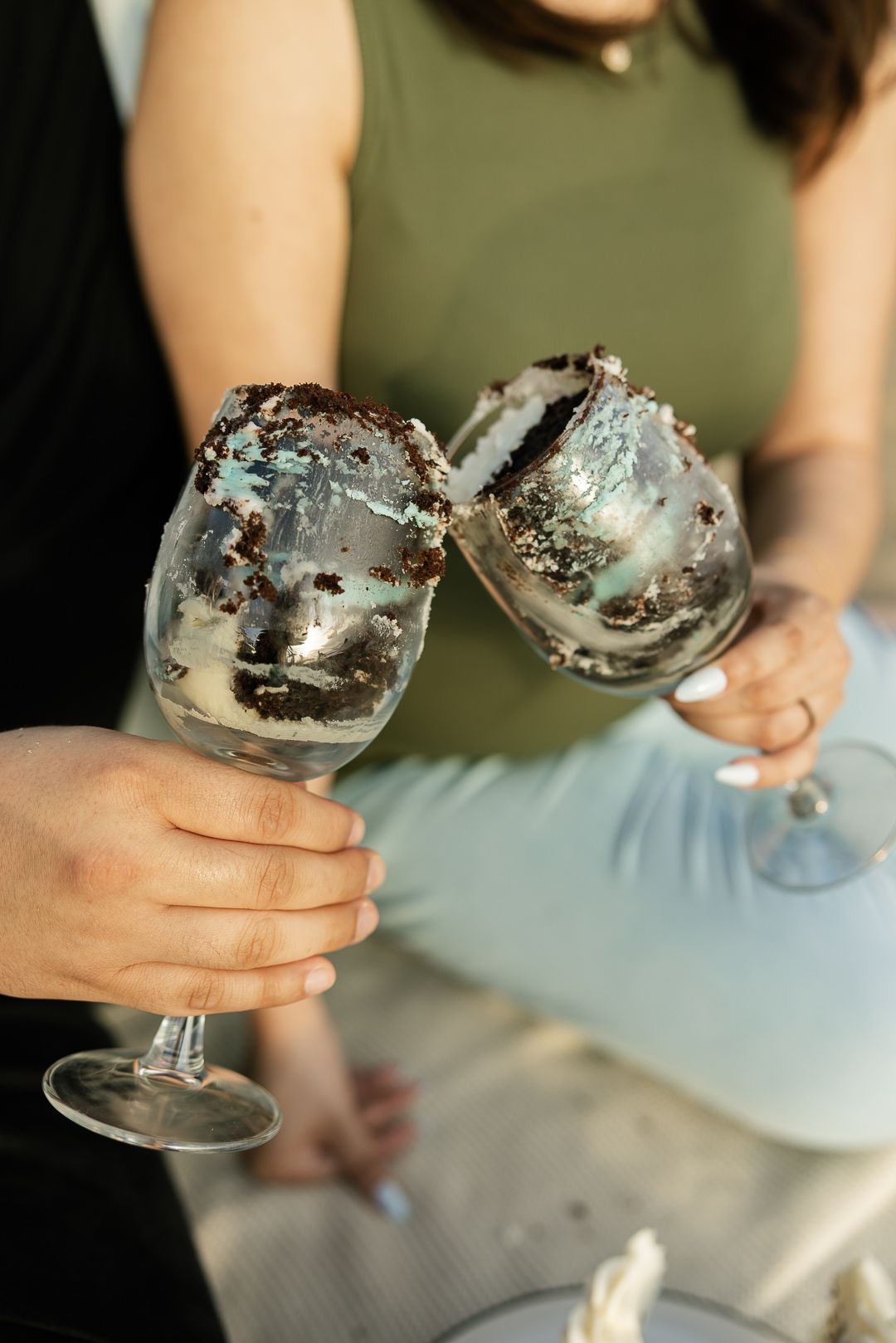 Two wine glasses filled with decadent chocolate and vanilla desserts topped with whipped cream and cookie crumbles.