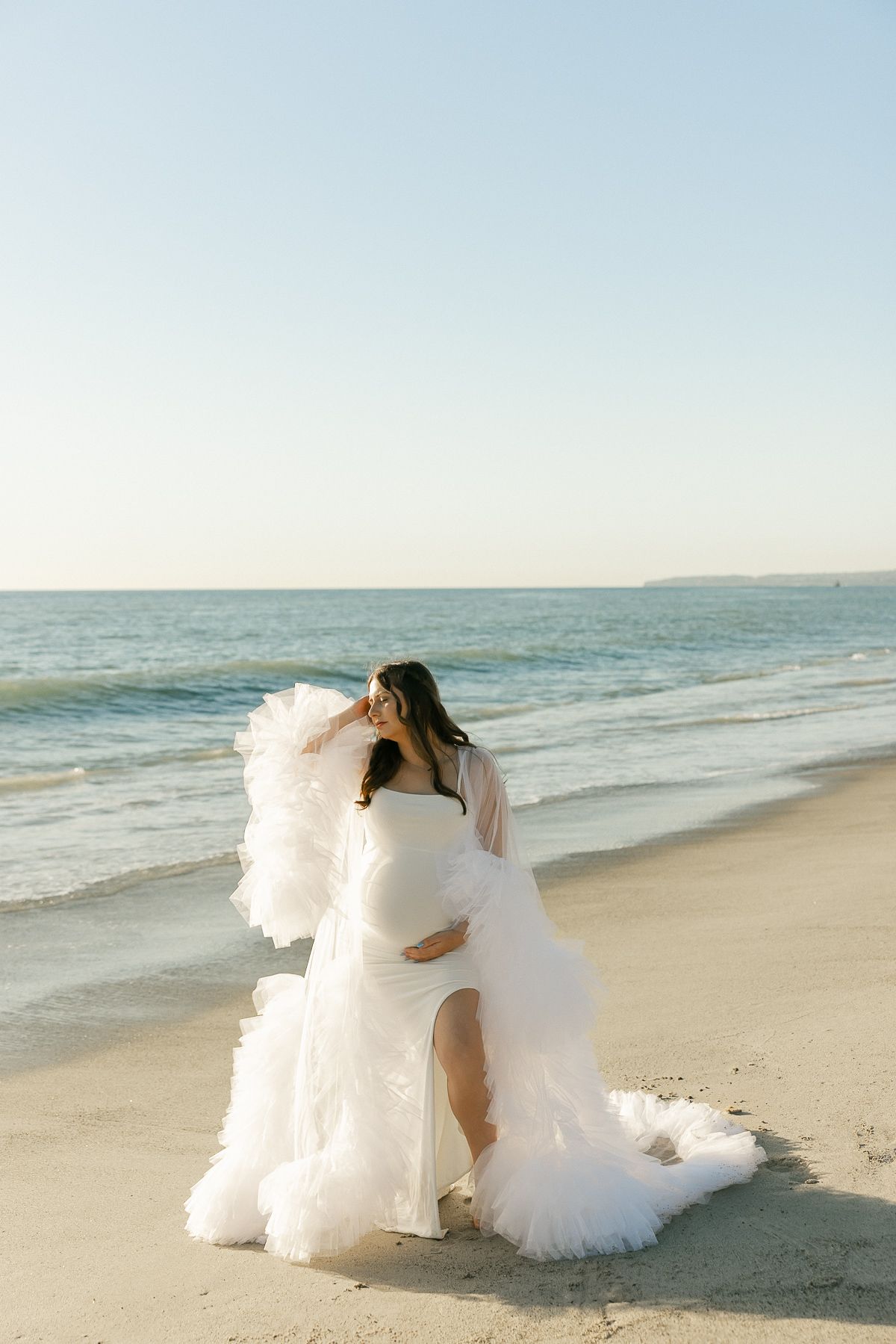 Dreamy bridal portraits on sandy beach with flowing white gown and ocean waves in background.