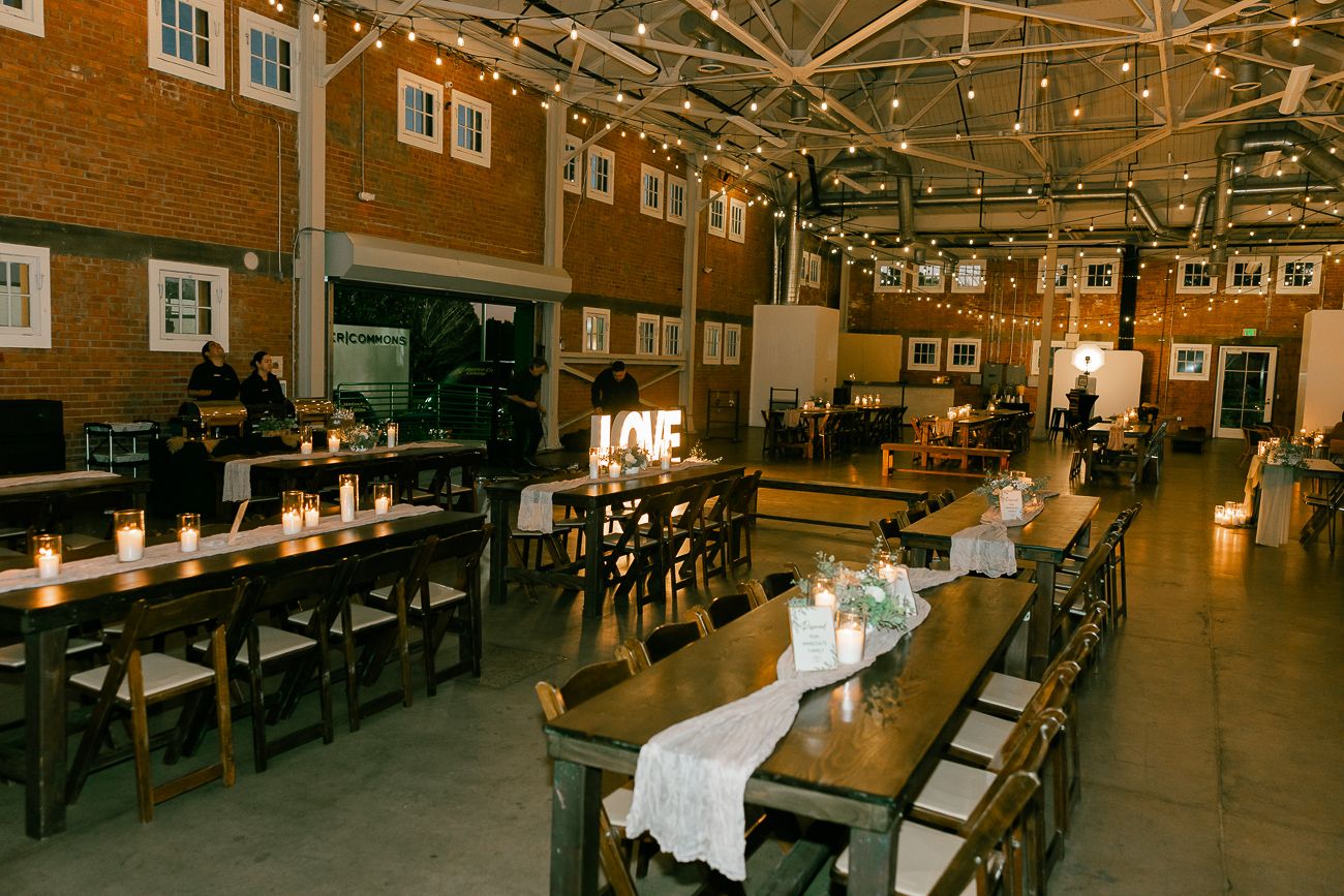 Rustic wedding reception venue with long wooden tables, string lights, and exposed brick walls.
